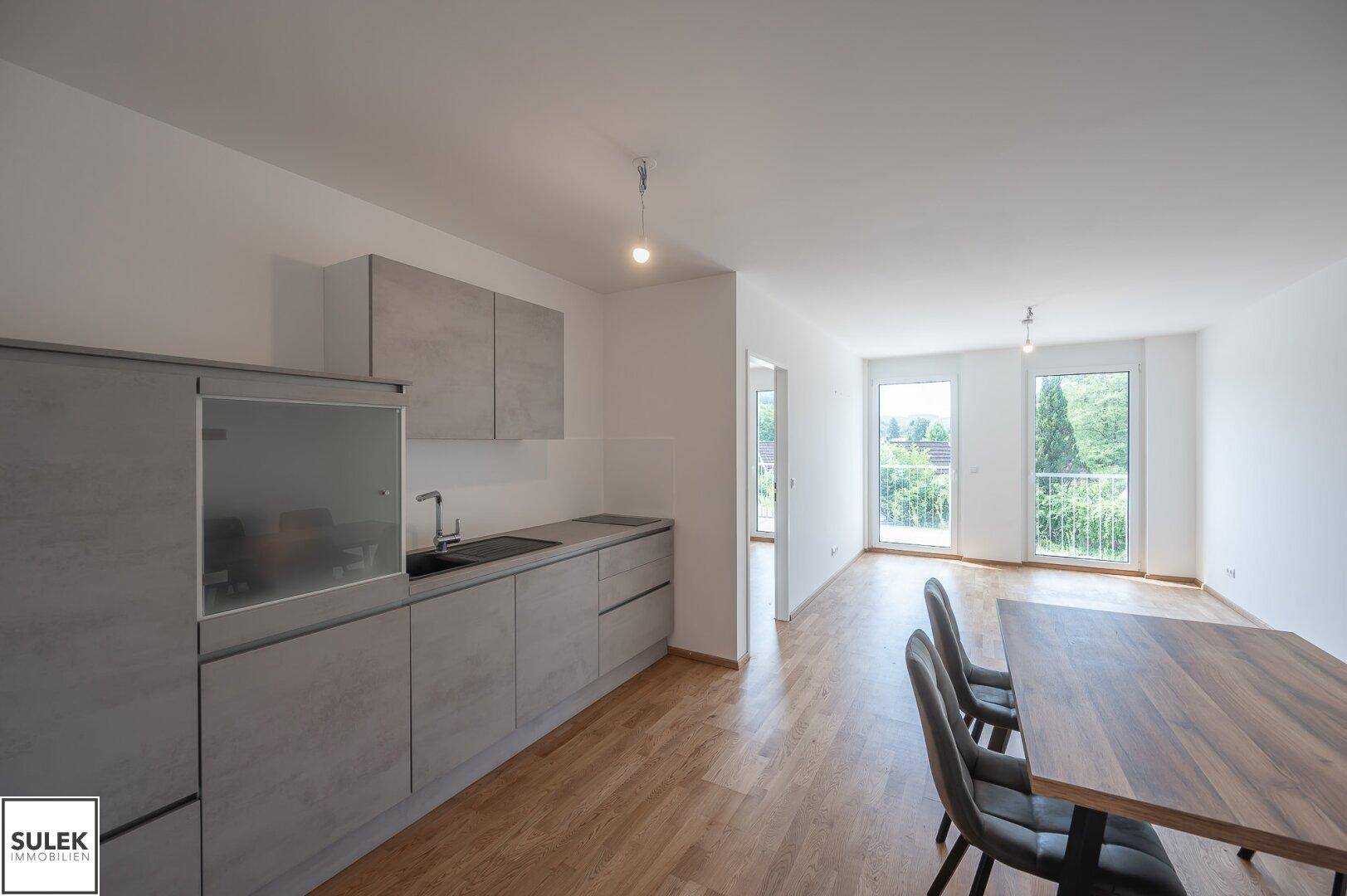 Offener Wohn-Essbereich mit moderner Küchenzeile, Esstisch und Zugang zum Balkon.