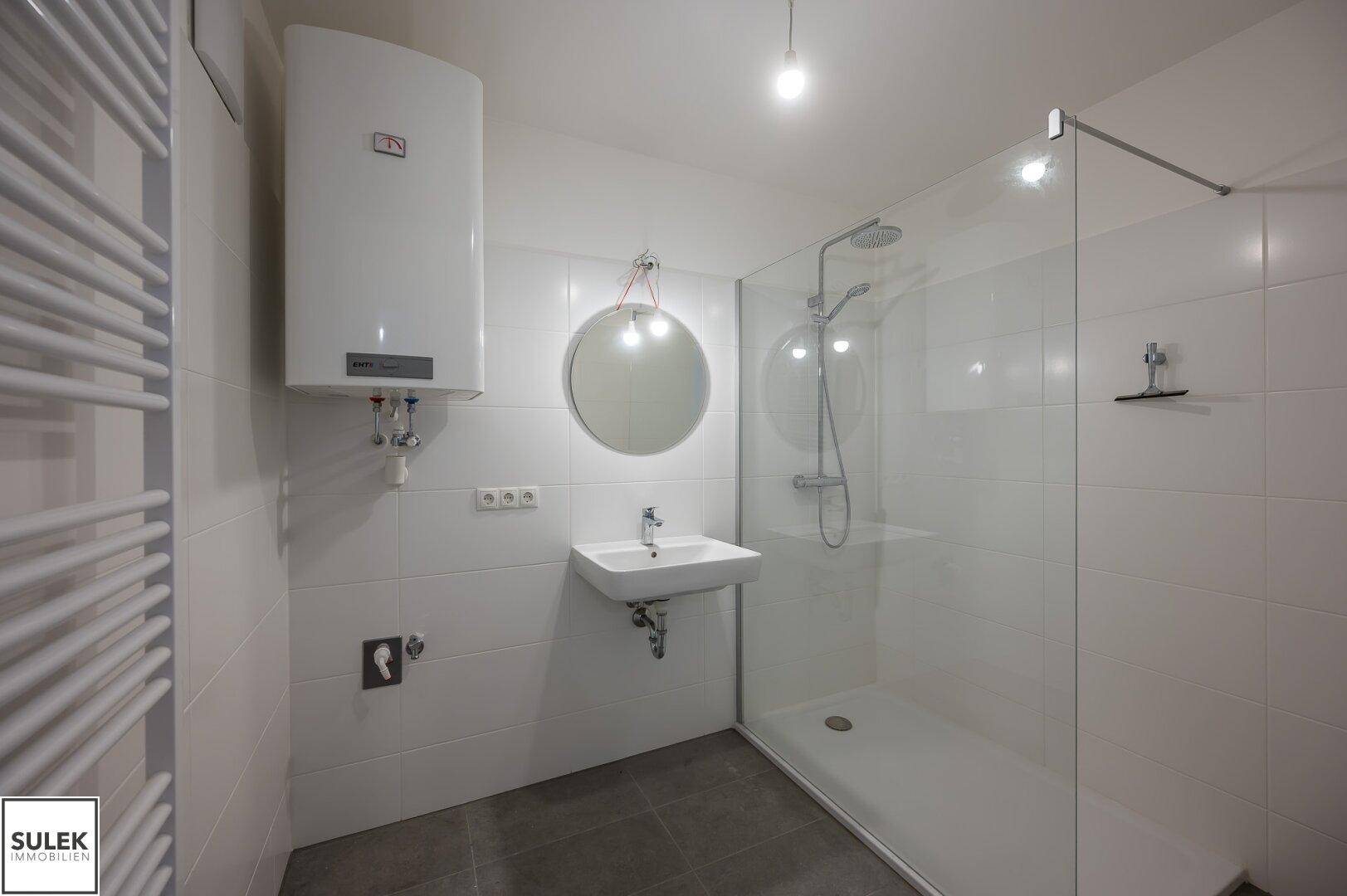 Modernes Badezimmer mit ebenerdiger Dusche, Waschbecken und Handtuchheizkörper.