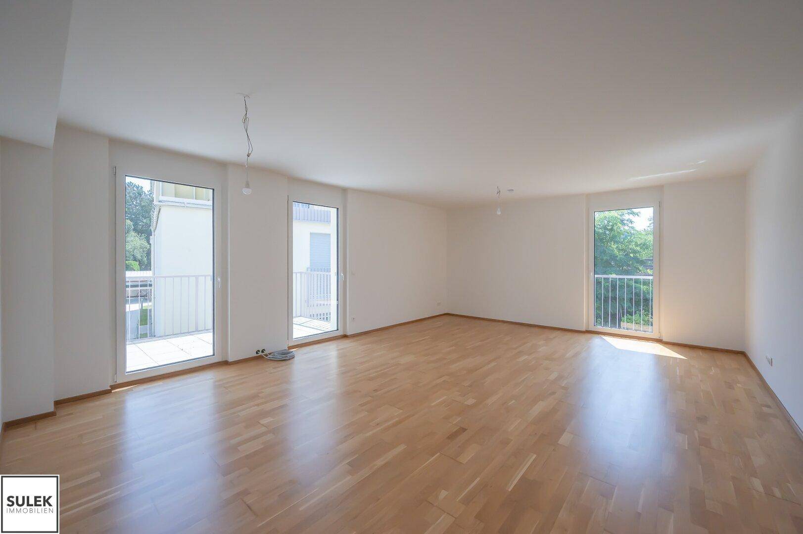 Helles, leeres Wohnzimmer mit Parkettboden und mehreren Zugängen zu französischen Balkonen.