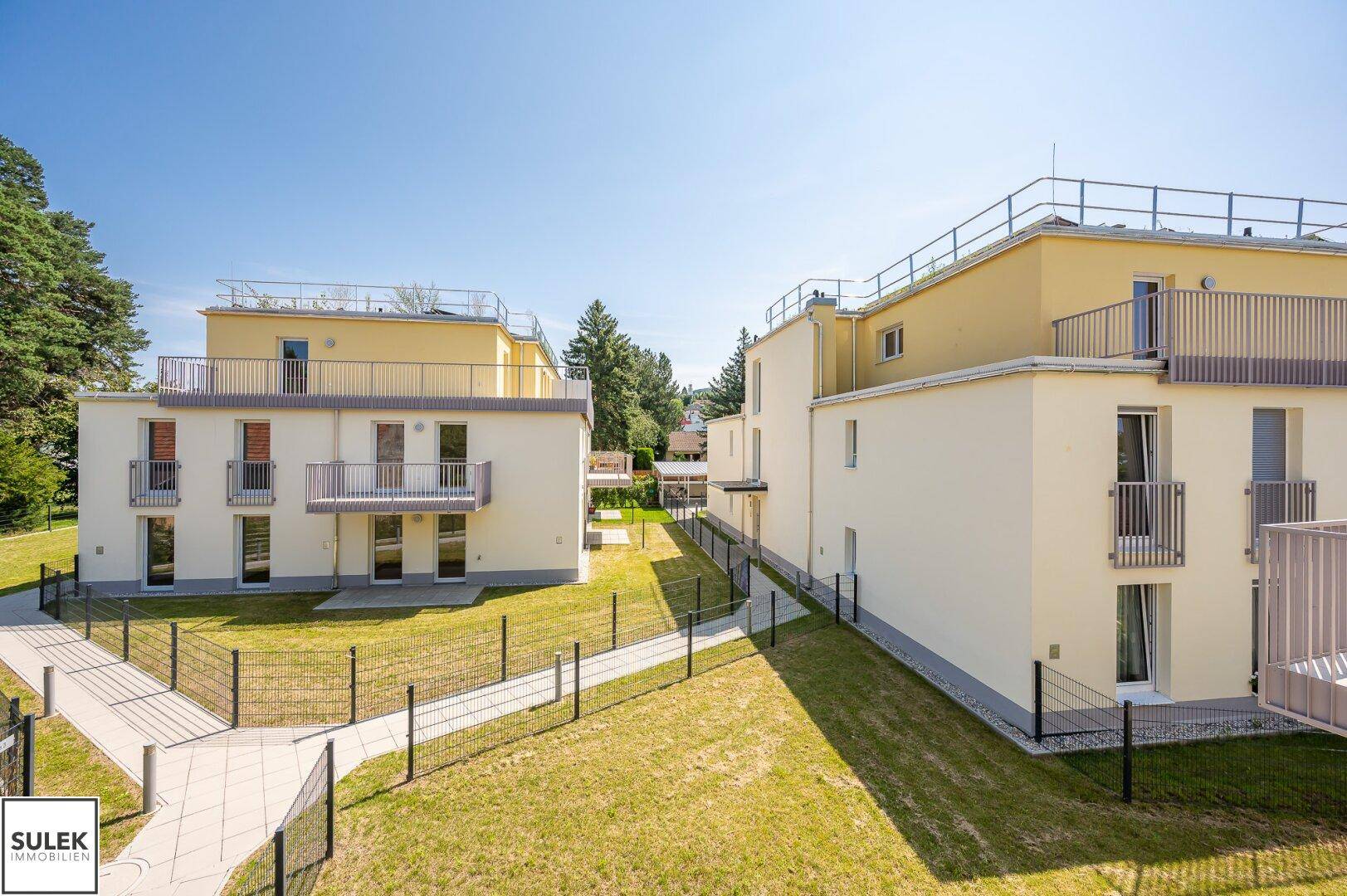 Moderne Wohngebäude mit hellen Fassaden, Balkonen und gepflegten Grünflächen dazwischen.
