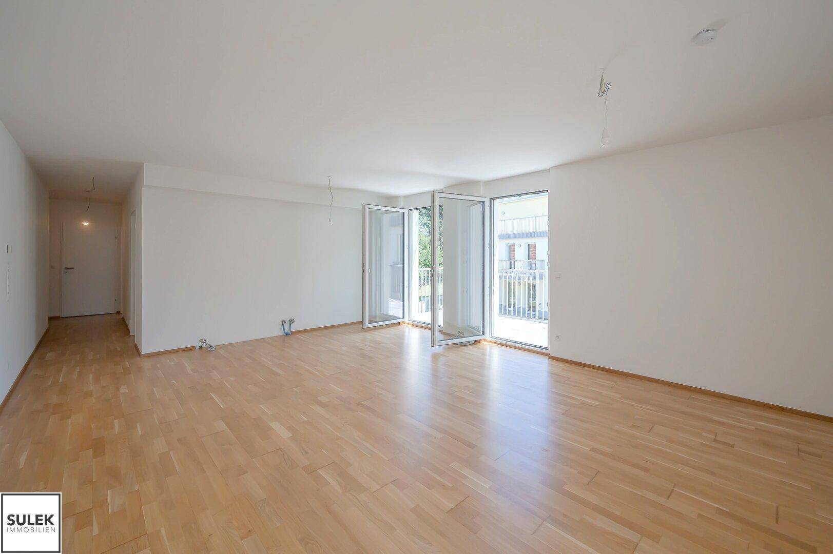 Geräumiges Wohnzimmer mit hellem Parkettboden und mehreren Fenstertüren für viel Tageslicht.