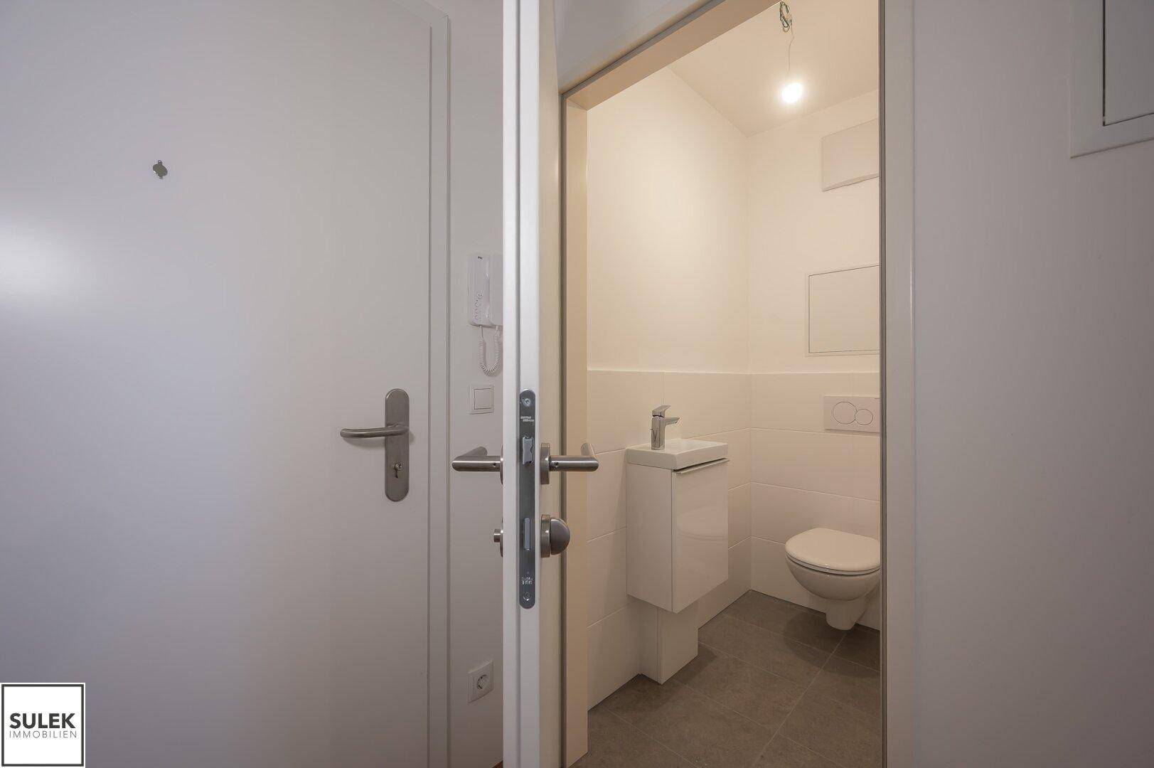 Modernes Gäste-WC mit weißen Fliesen, wandhängendem WC und kleinem Waschbecken.