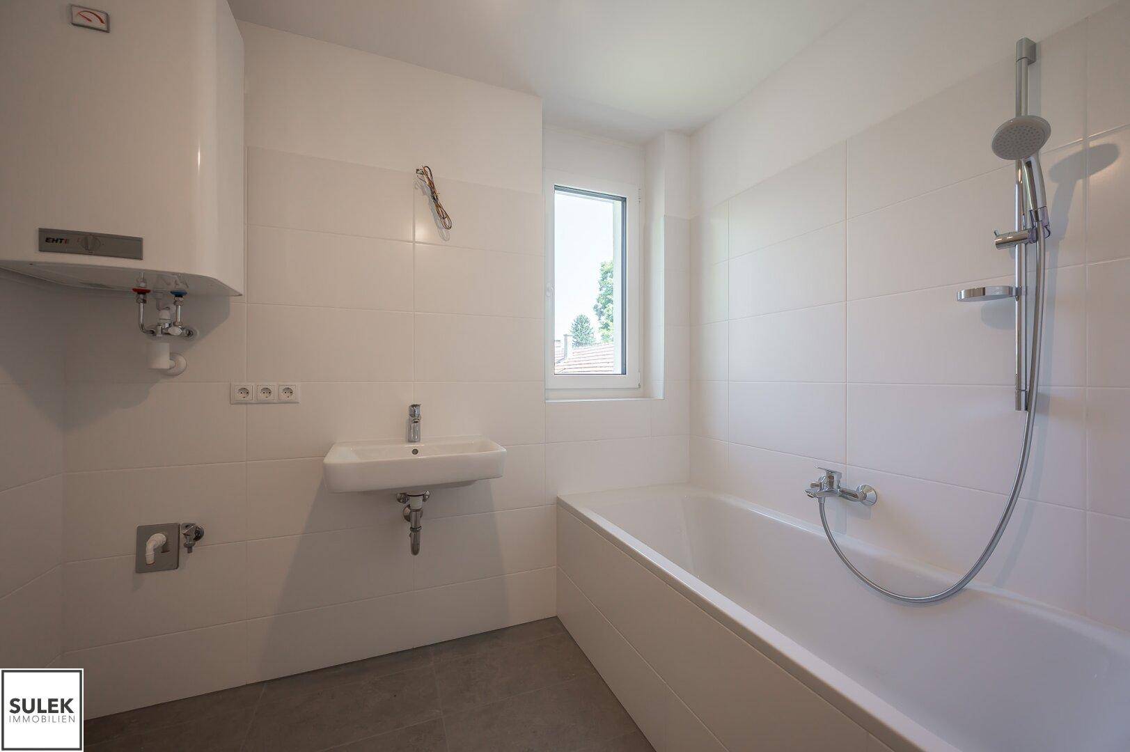 Helles Badezimmer mit weißen Fliesen, Badewanne, Waschbecken und Fenster für natürliche Belüftung.