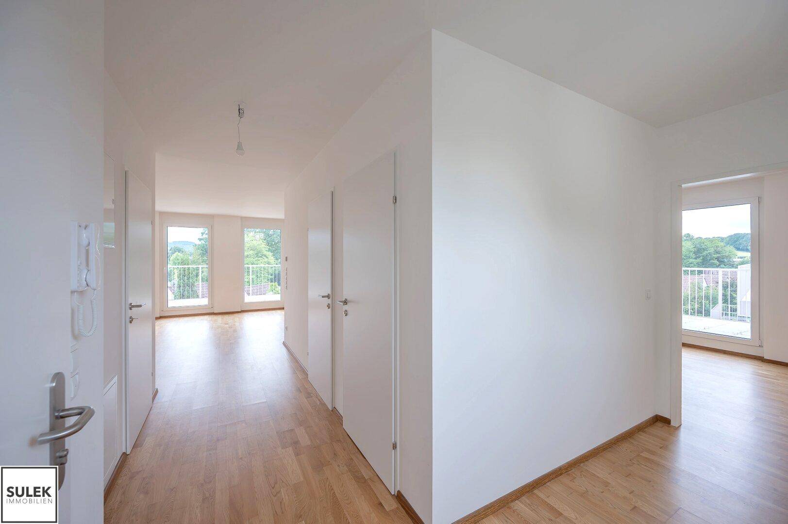 Heller Flur mit Parkettboden und weißen Türen, der zu verschiedenen Räumen und einem Balkon führt.