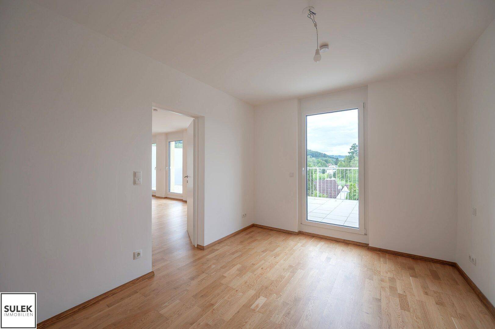 Helles Zimmer mit Parkettboden und Zugang zu einem Balkon, bietet viel Tageslicht und frische Luft.