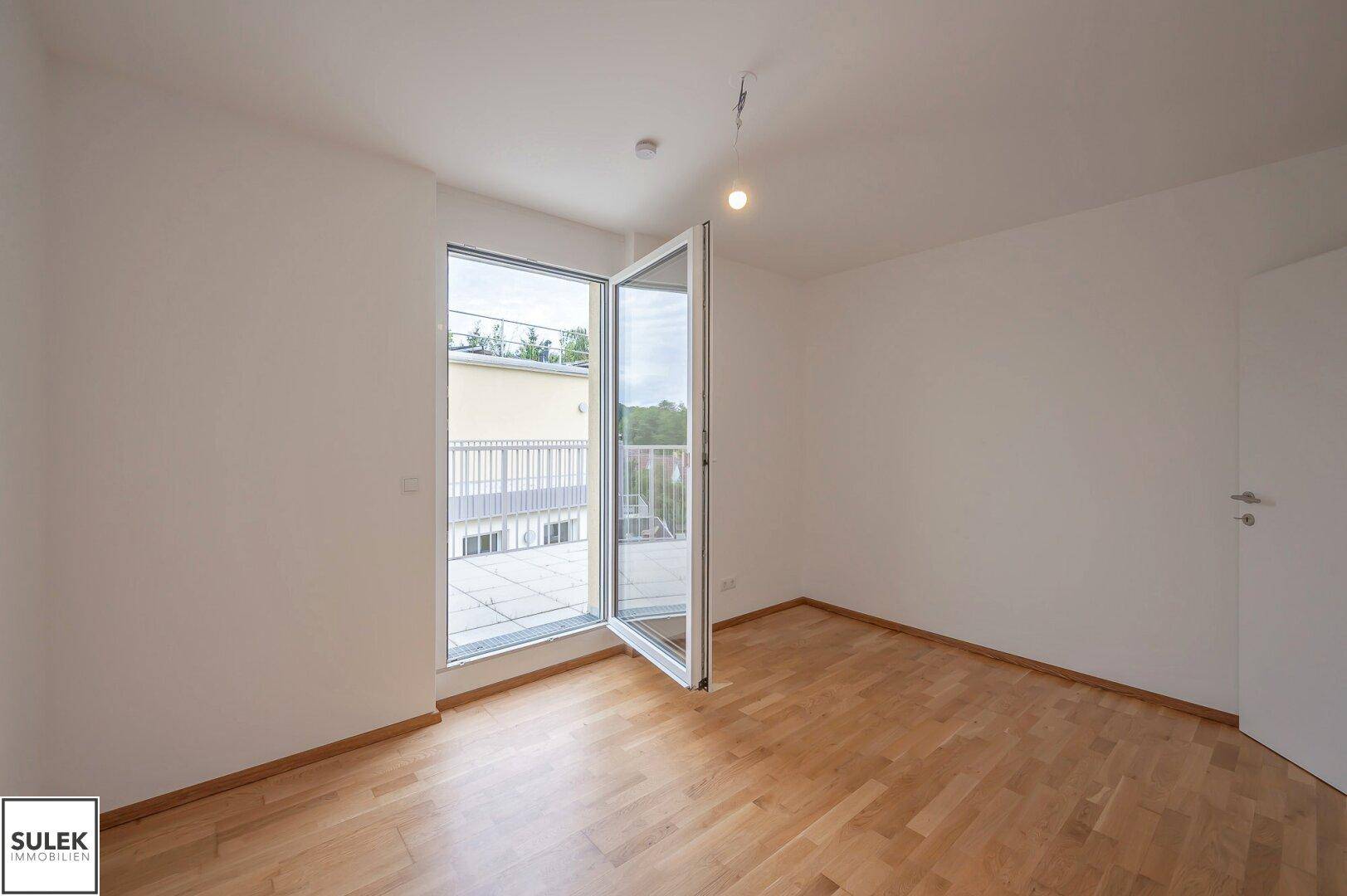 Helles Schlafzimmer mit Parkettboden und direktem Zugang zu einem Balkon, bietet eine angenehme Atmosphäre.