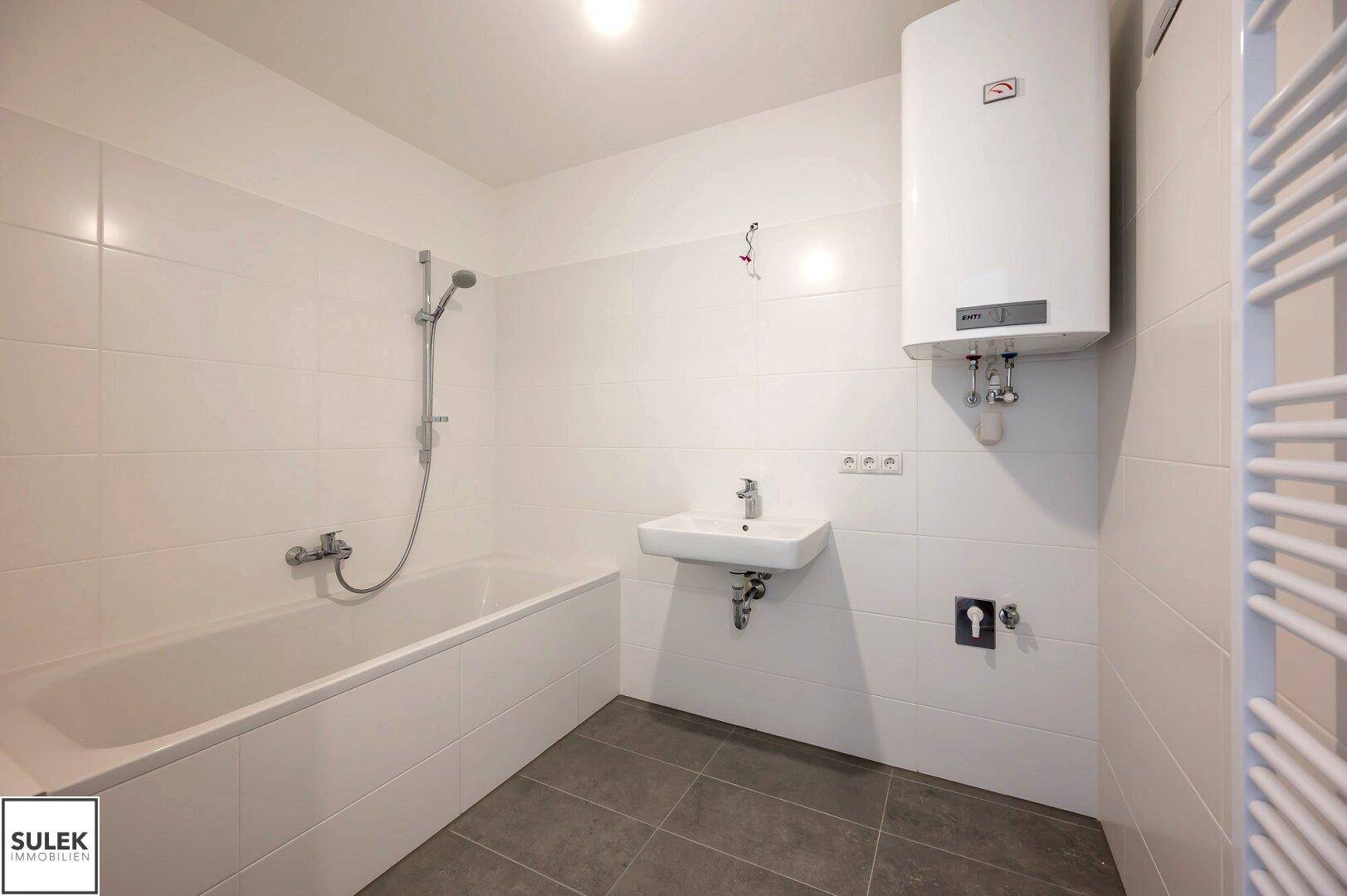 Helles Badezimmer mit Badewanne, Waschbecken und Handtuchheizkörper, komplett gefliest und funktional.