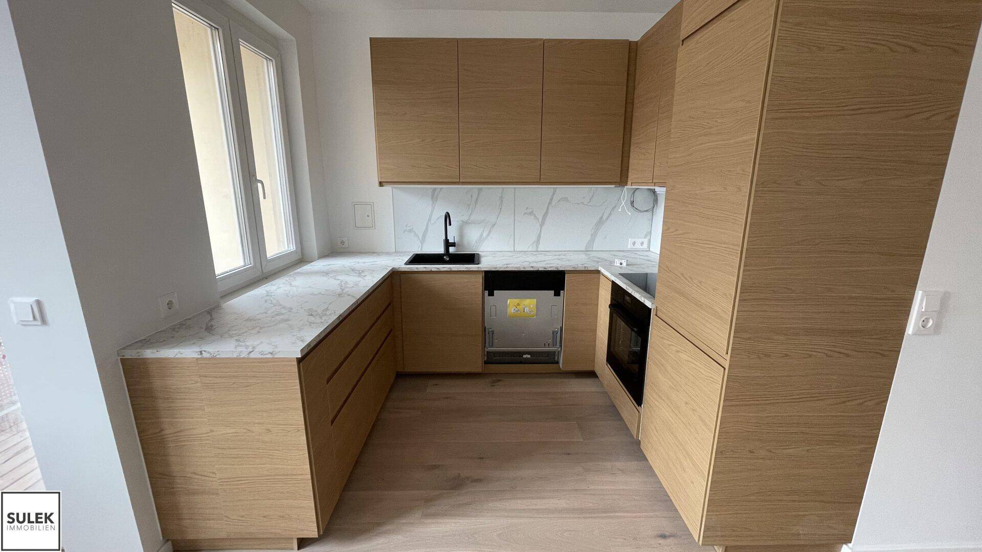 Moderne Küche mit hellen Holzfronten, Marmorarbeitsplatten und integrierten Geräten, inklusive Fenster.