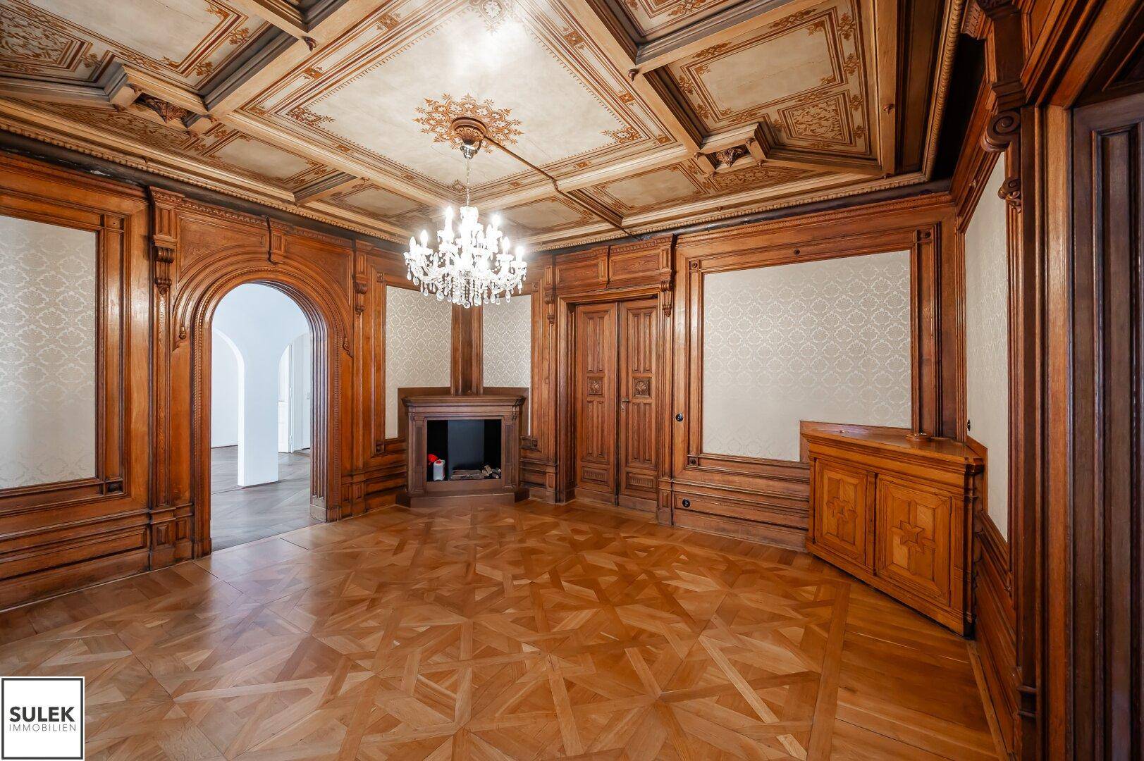 Prunkvolles Wohnzimmer mit aufwendigen Holzvertäfelungen, Parkettboden und Kronleuchter.