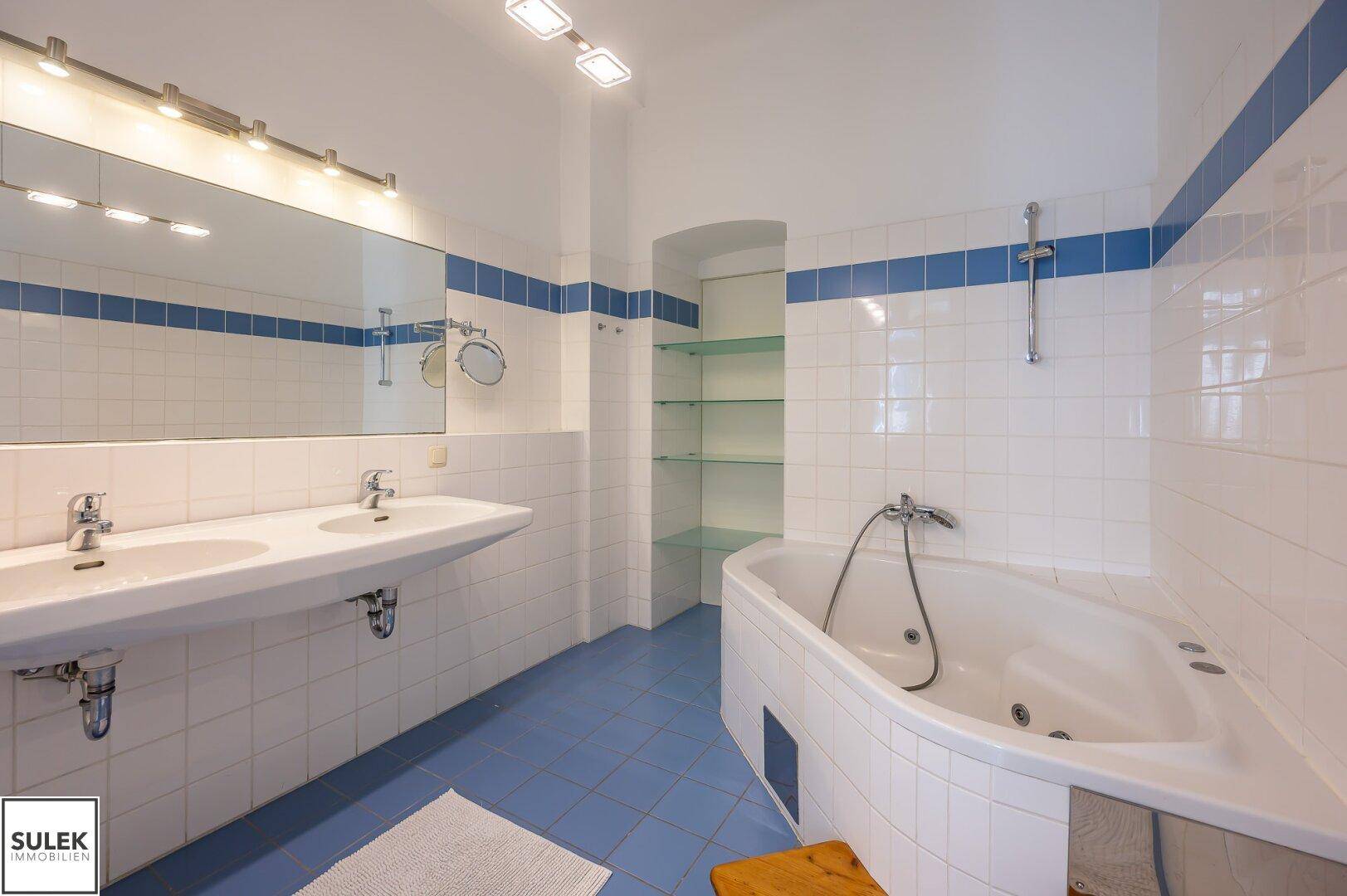 Geräumiges Badezimmer mit Eck-Whirlpool, Doppelwaschbecken und weiß-blauen Fliesen.