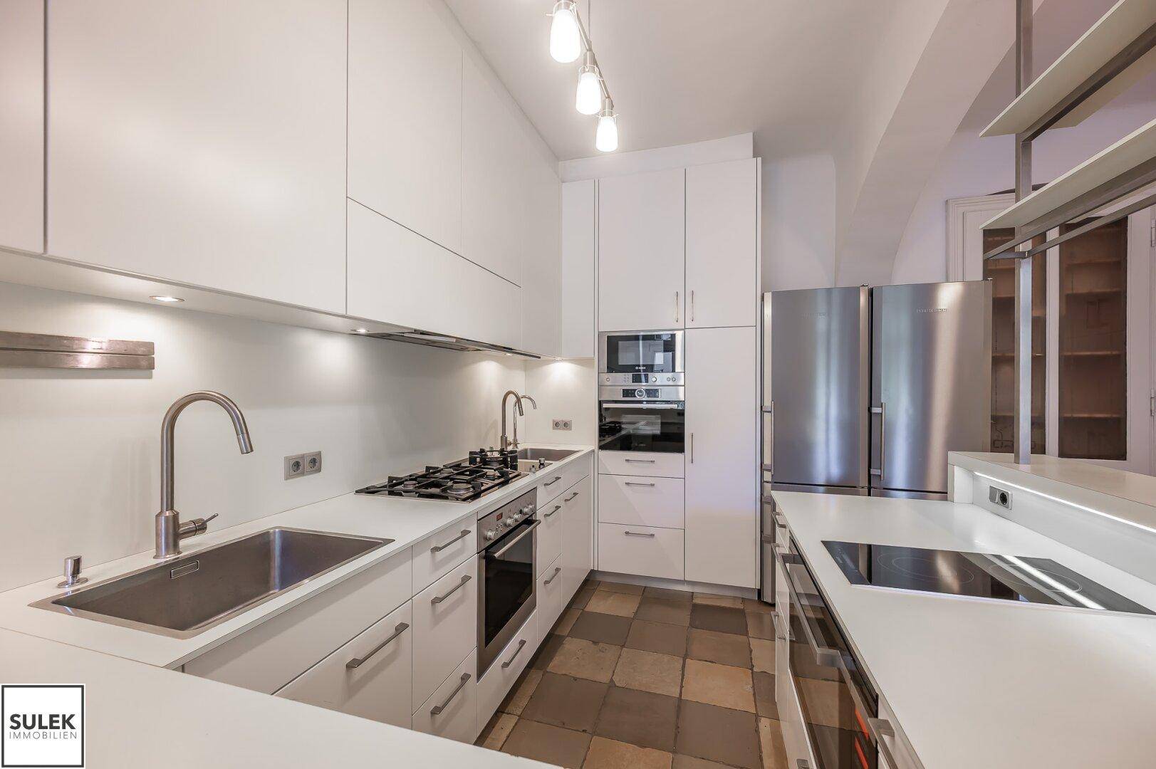 Moderne weiße Küche mit integrierten Geräten, zwei Spülbecken und Induktionskochfeld.