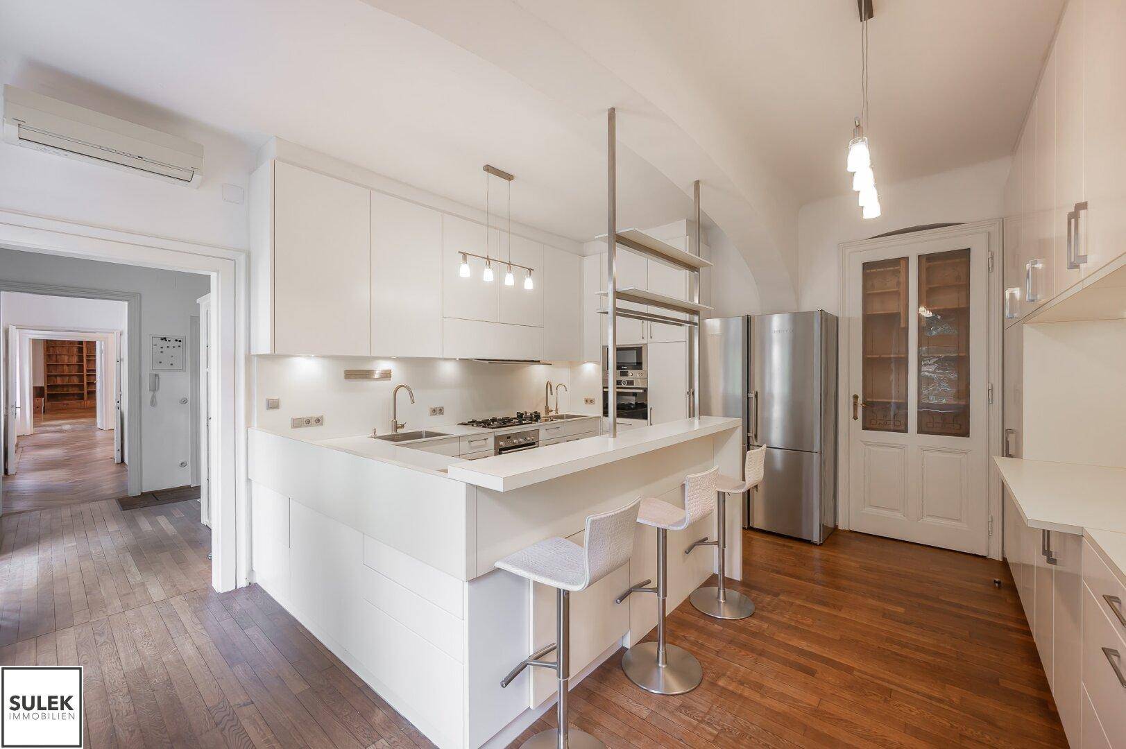 Offene weiße Küche mit Frühstücksbar, Kühlschrank und Blick in den angrenzenden Wohnbereich.