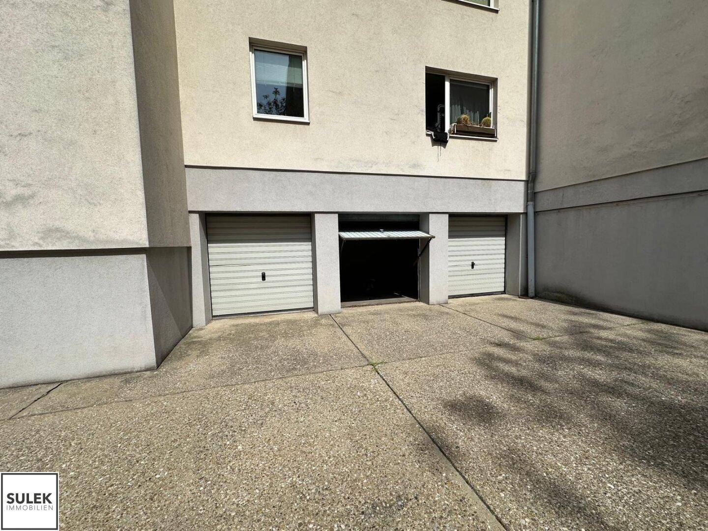 Gebäudefassade mit zwei Garagentoren und einem offenen Zugang zu einem weiteren Stellplatz.