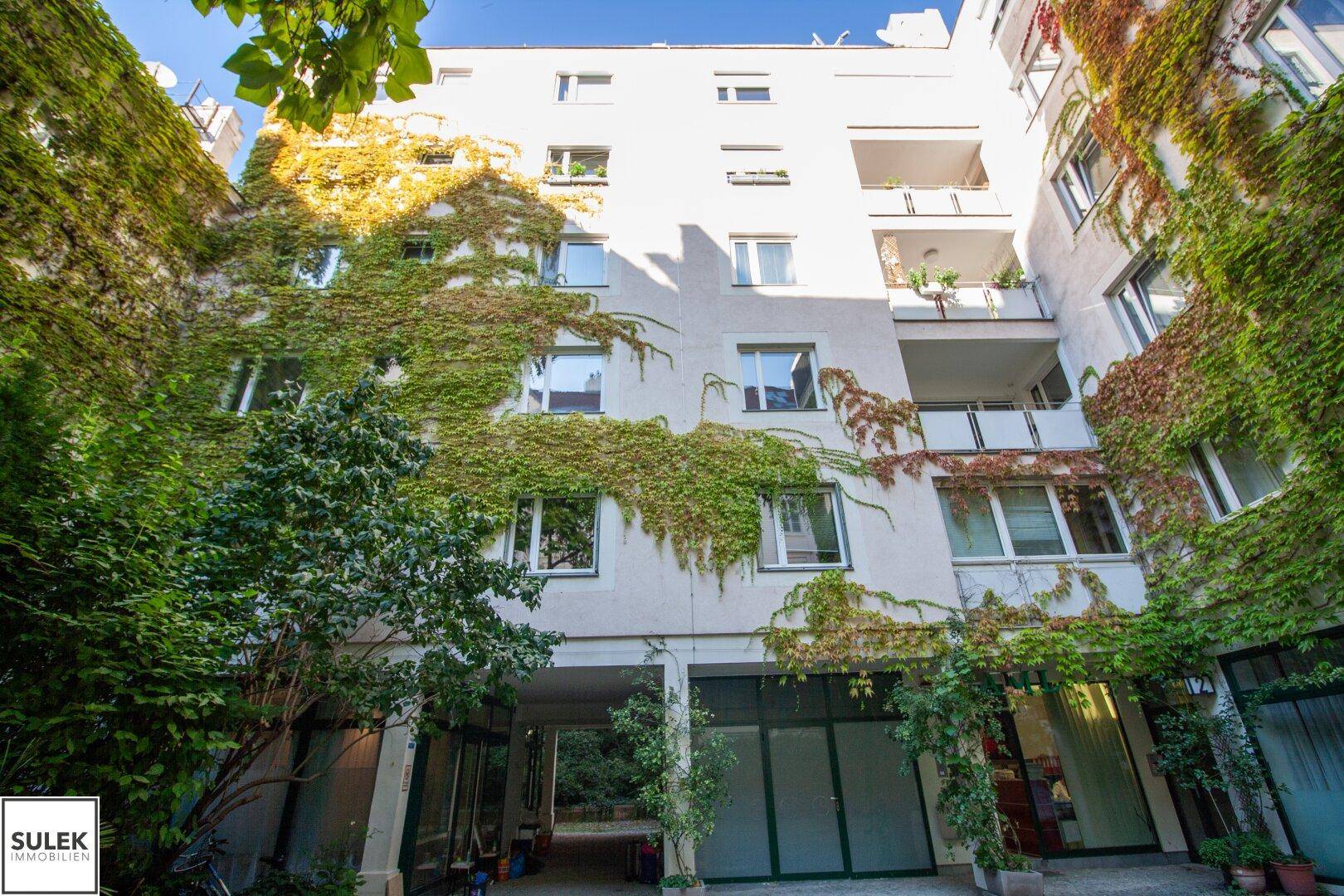 Mehrstöckiges Gebäude mit begrünten Fassaden und Balkonen, umgeben von üppiger Vegetation.
