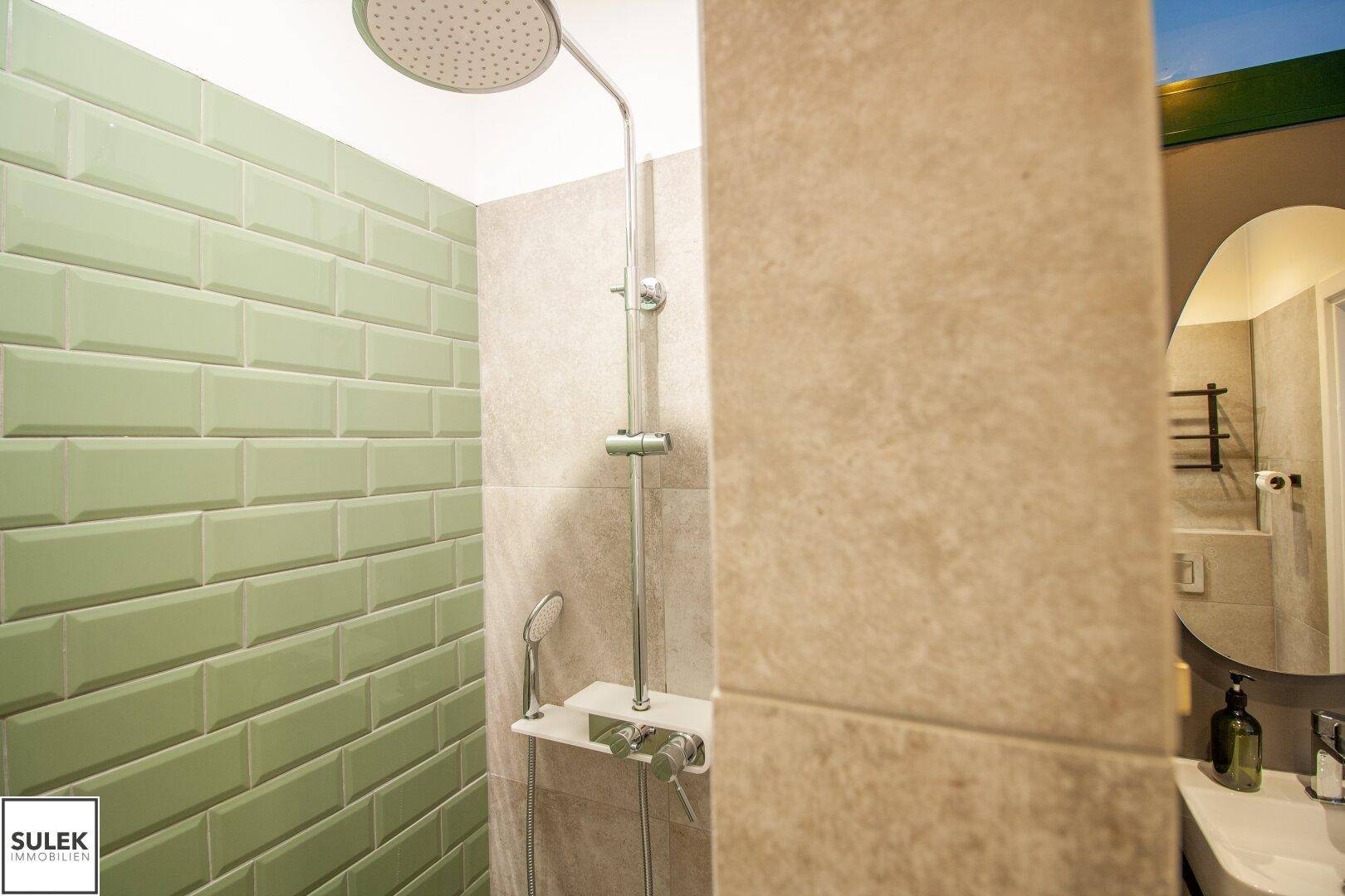 Detaillierte Ansicht einer modernen Regendusche mit hellgrünen Fliesen und beigefarbenen Wänden.