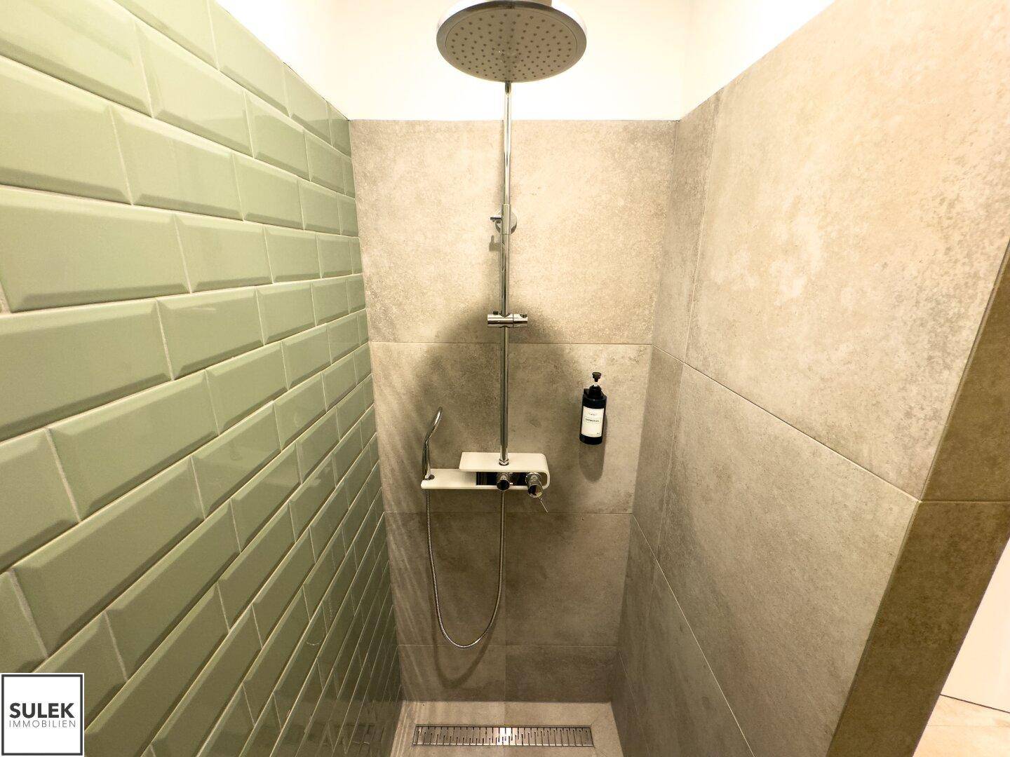 Moderne Dusche mit Regenduschkopf, hellgrünen Fliesen und neutralen Wandfliesen.