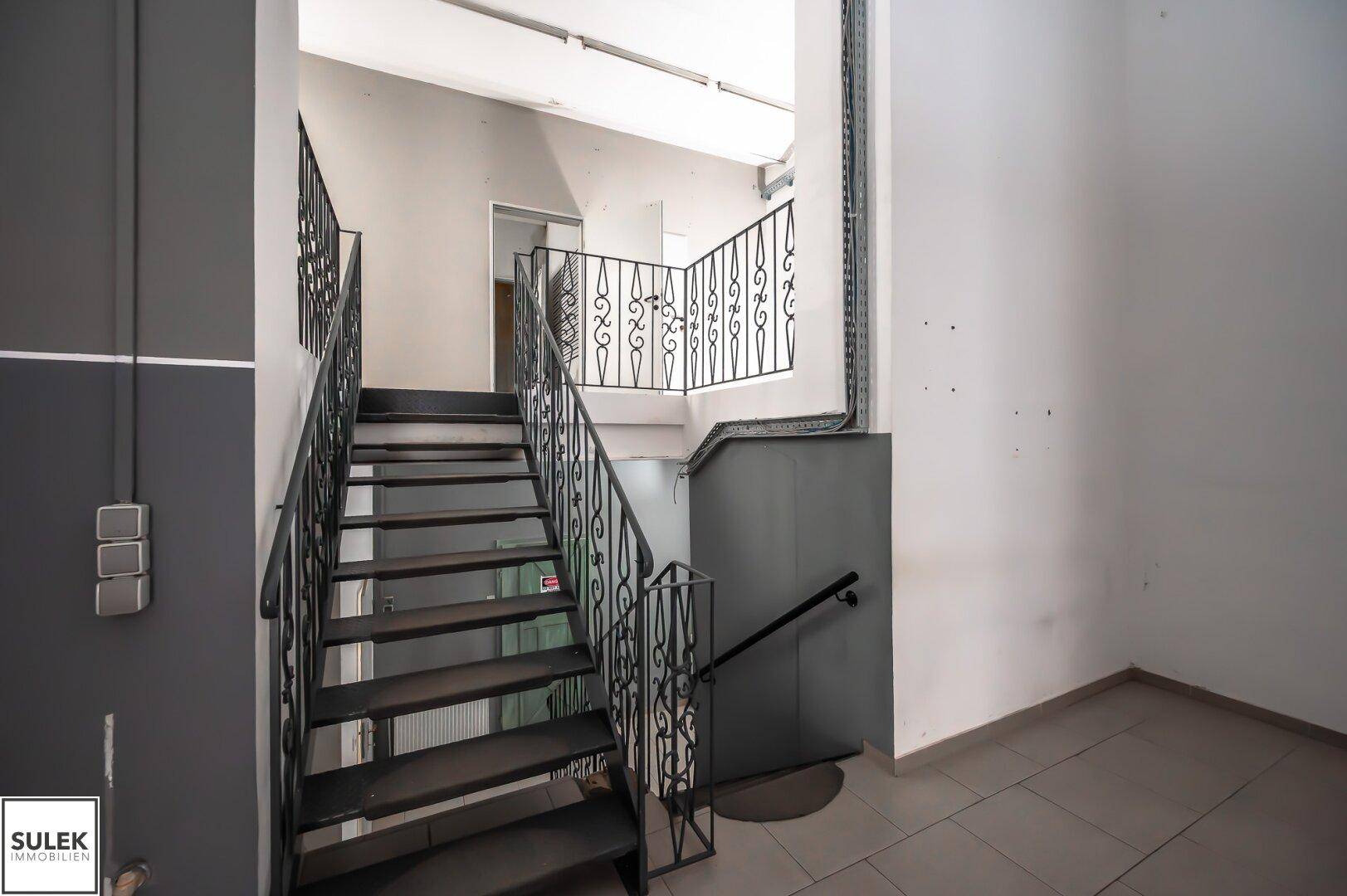 Detailansicht einer schmiedeeisernen Treppe mit Fliesenboden und schlichten Wänden in einem Gewerbegebäude.