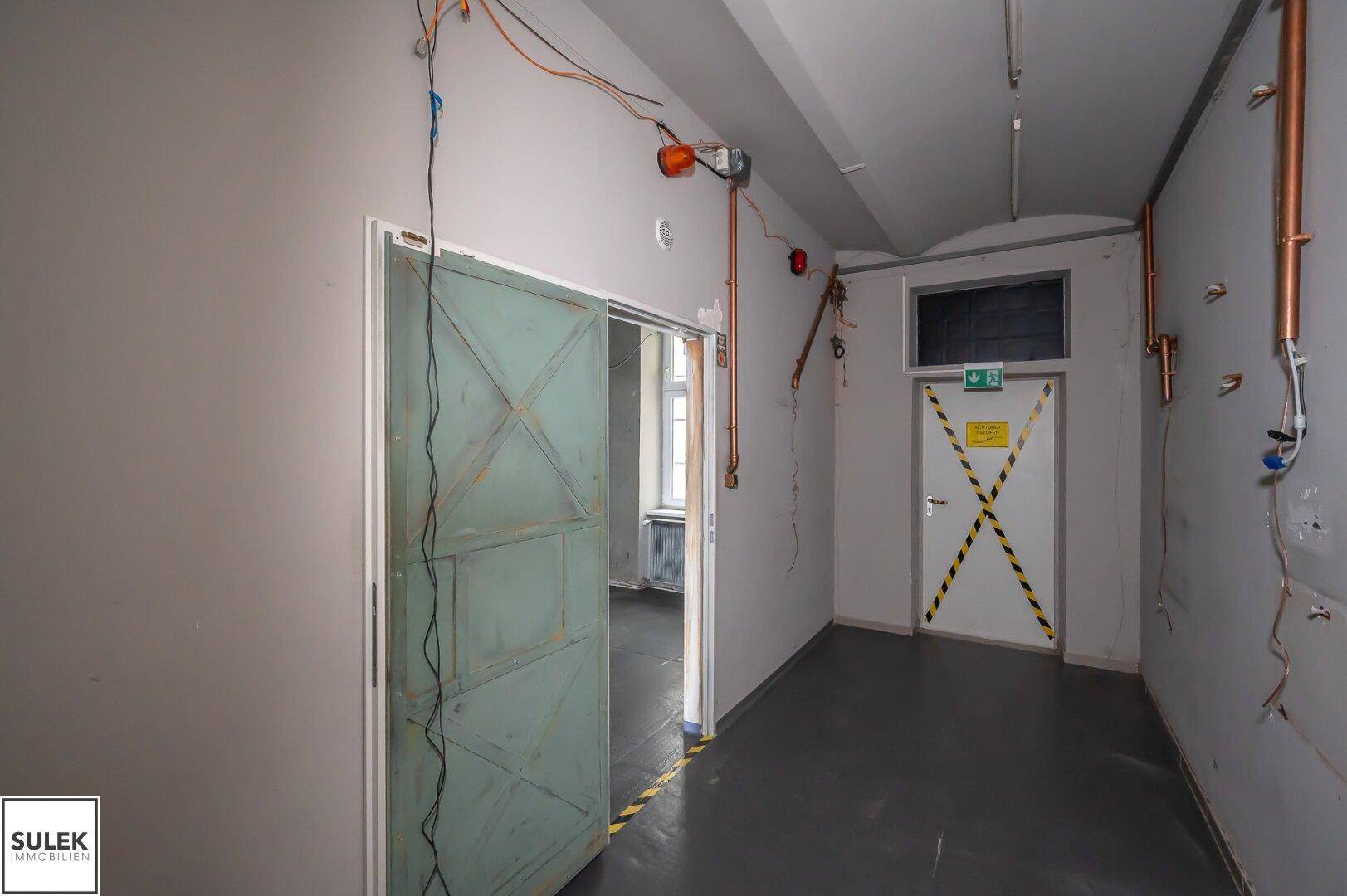 Flur mit dunklem Boden, sichtbaren Kupferrohren und einer Schiebetür zu einem weiteren Raum.