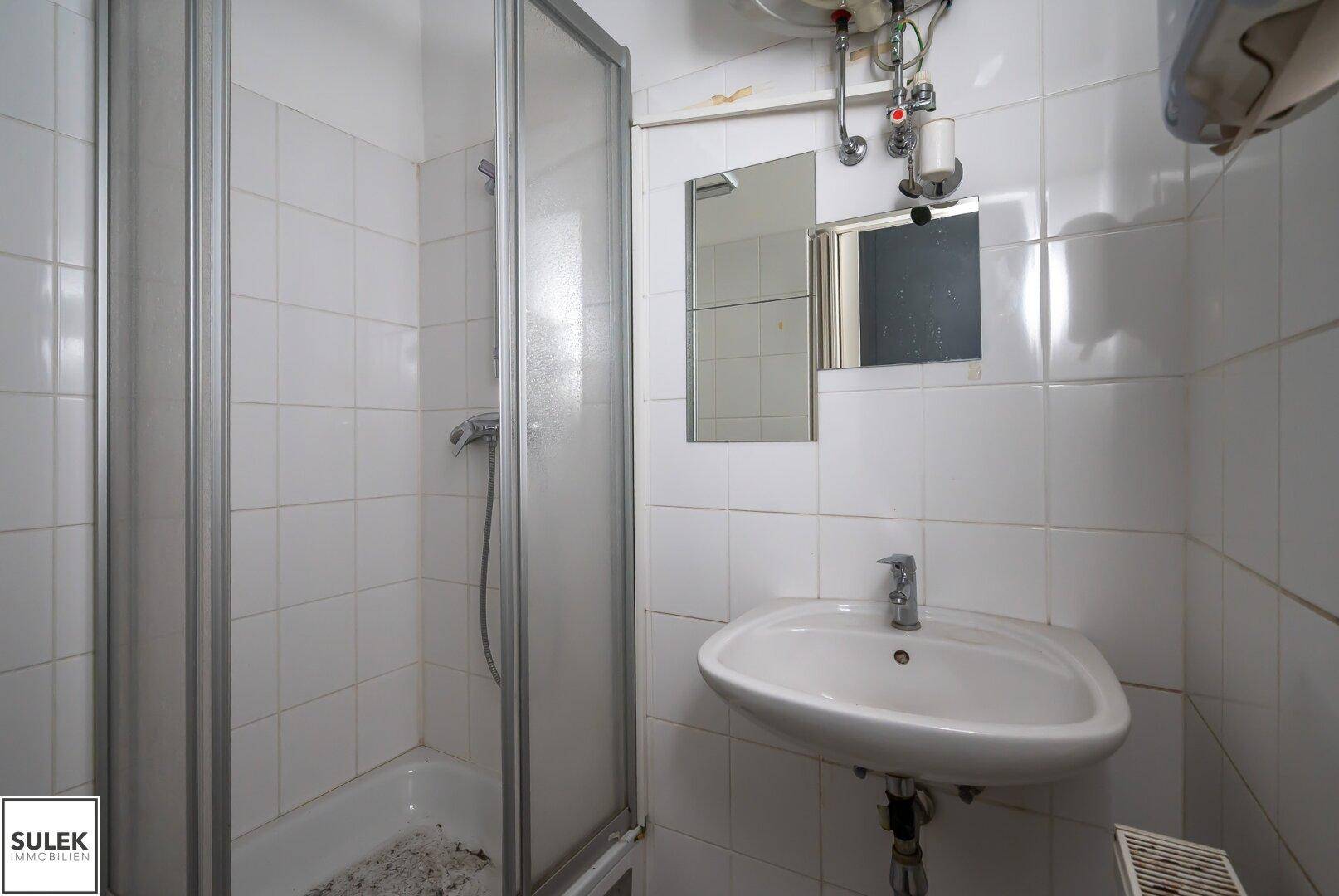 Kleines Badezimmer mit Duschkabine, Waschbecken und weißen Fliesen an den Wänden.