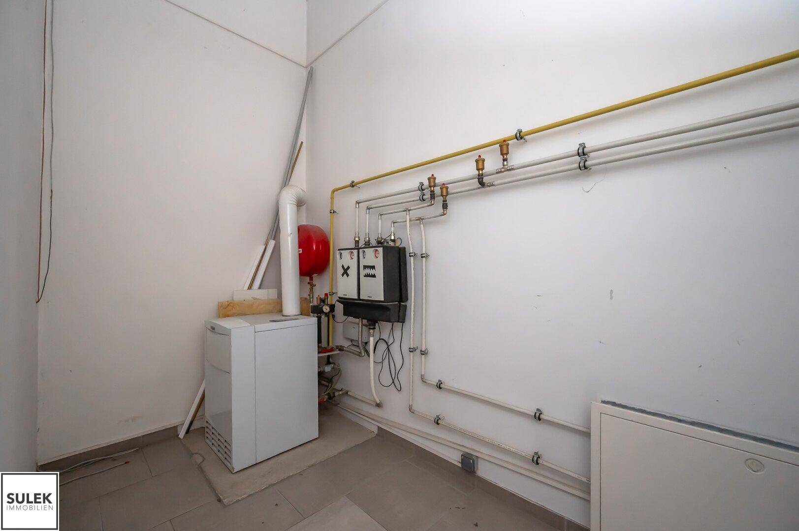 Technikraum mit Heizungsanlage, sichtbaren Rohren und einem Boiler an der Wand.