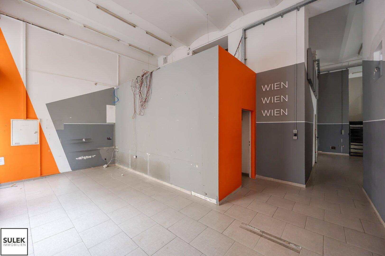 Großer Gewerberaum mit Fliesenboden, orangefarbenen und grauen Wänden und einem Schriftzug "WIEN".