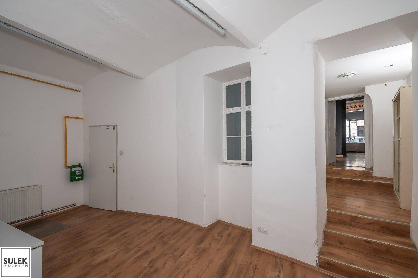 Gewerberaum mit gewölbter Decke, Holzfußboden und einem Fenster, das natürliches Licht hereinlässt.