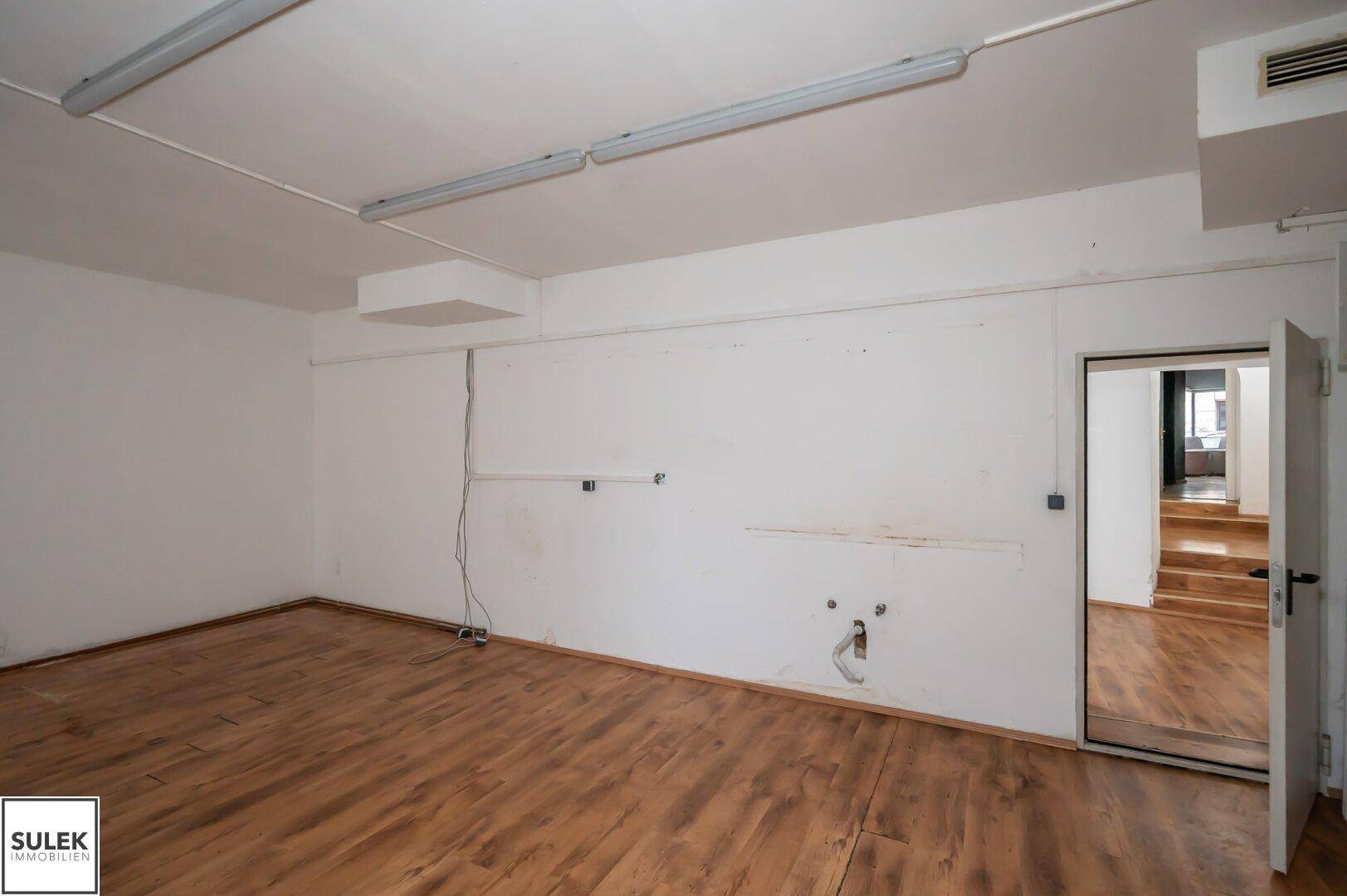 Geräumiger Gewerberaum mit Holzfußboden, weißen Wänden und Deckenbeleuchtung, bereit zur Nutzung.