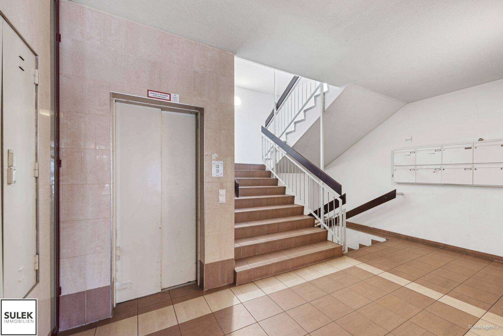 Treppenhaus mit Aufzug und Fliesenboden, führt zu den oberen Etagen des Gebäudes.