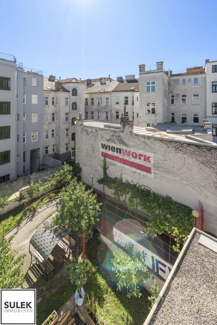 Blick von oben auf einen begrünten Innenhof mit Gebäuden und einer Werbefläche an der Wand.