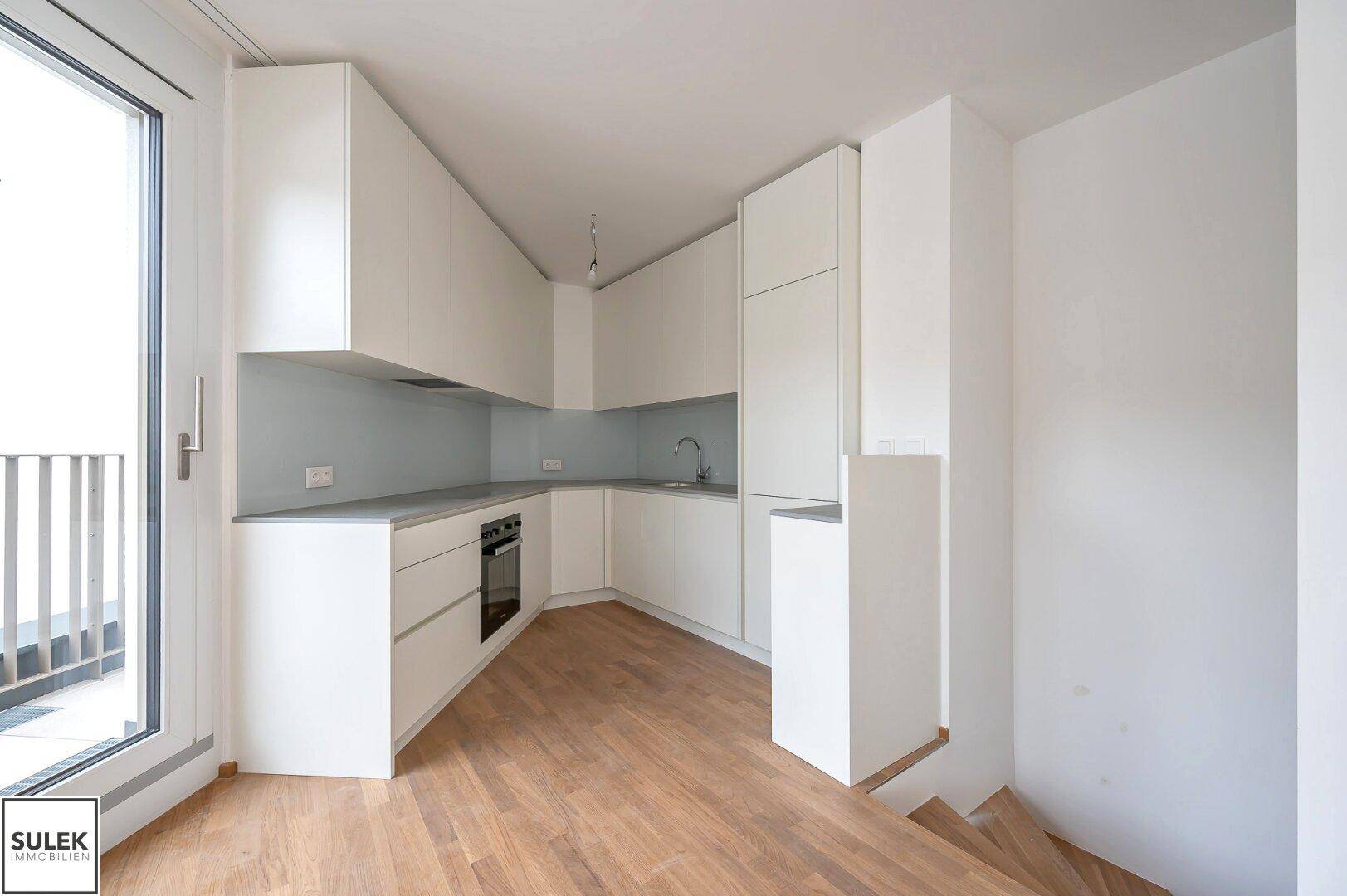 Moderne, unbenutzte Küche mit weißen Schränken, integrierten Geräten und Holzboden.