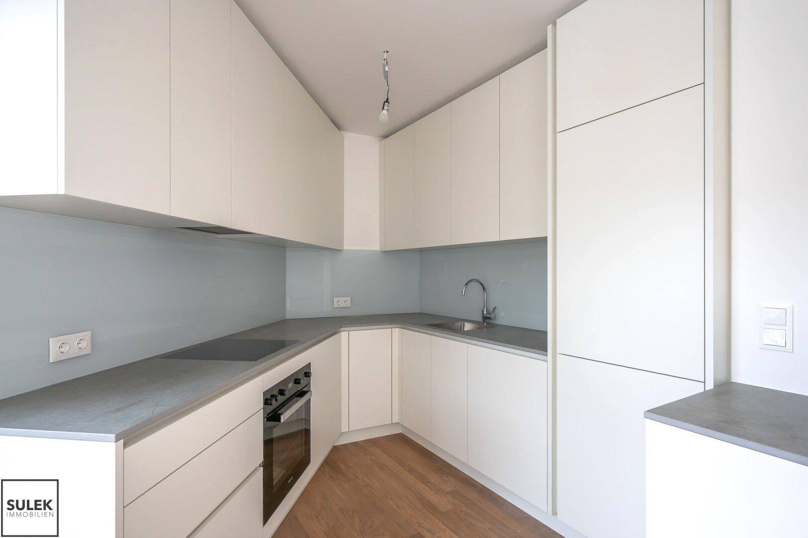 Neue, moderne Küche mit weißen Schränken, grauen Arbeitsplatten und integriertem Backofen.