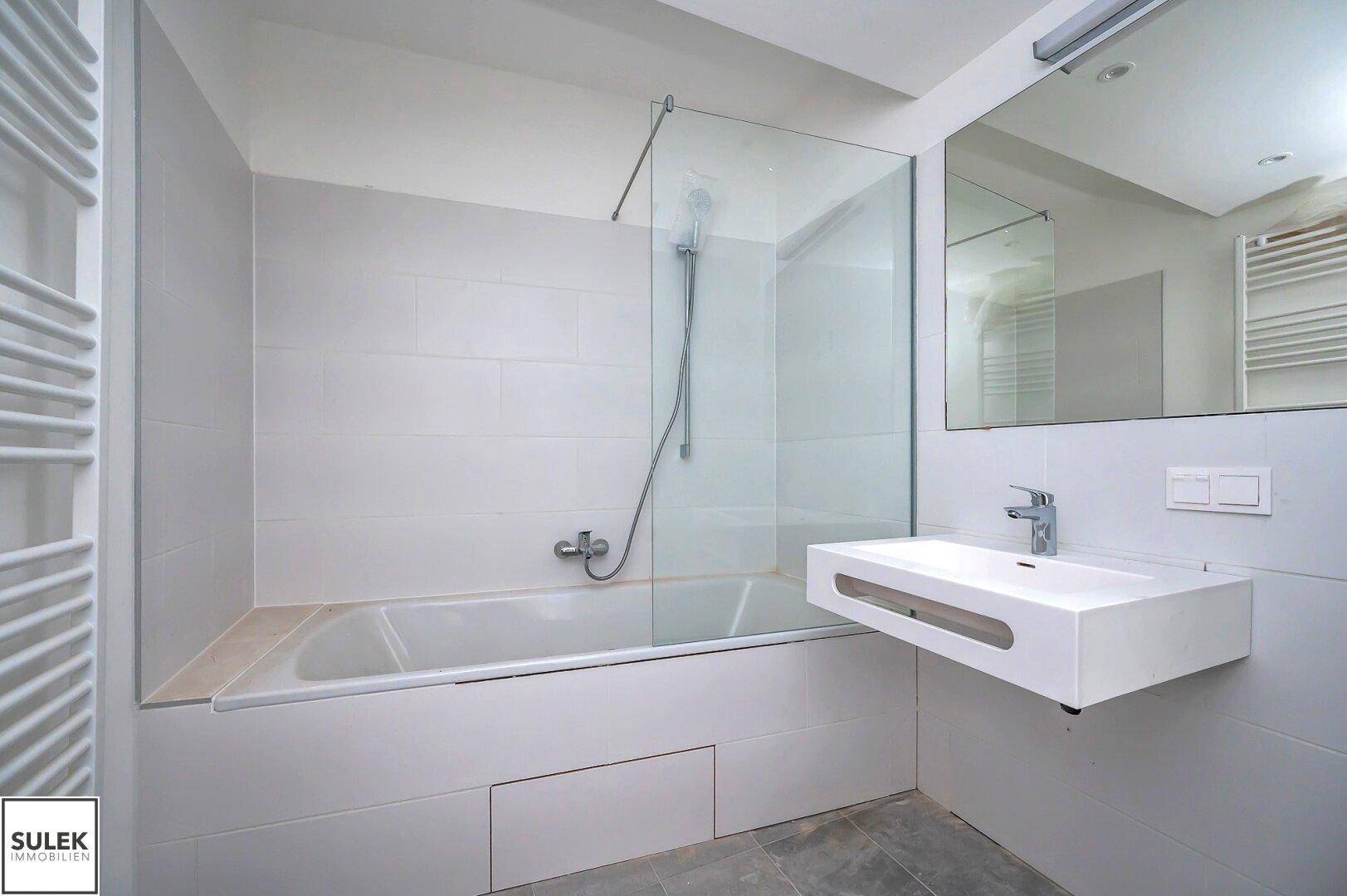 Modernes Badezimmer mit Badewanne, Glasduschwand, wandhängendem Waschbecken und beheiztem Handtuchhalter.