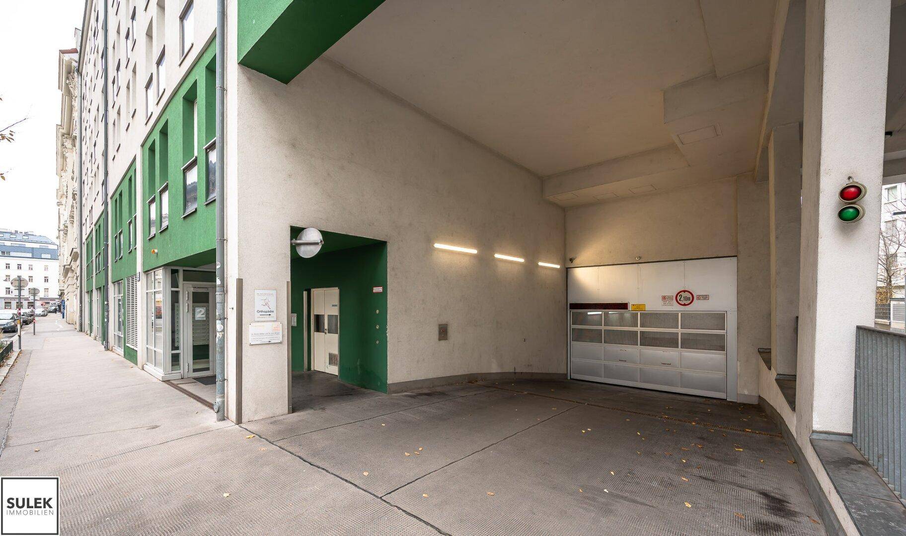 Einfahrt zu einer Tiefgarage mit Rolltor und Ampelsystem an einem modernen Gebäude.