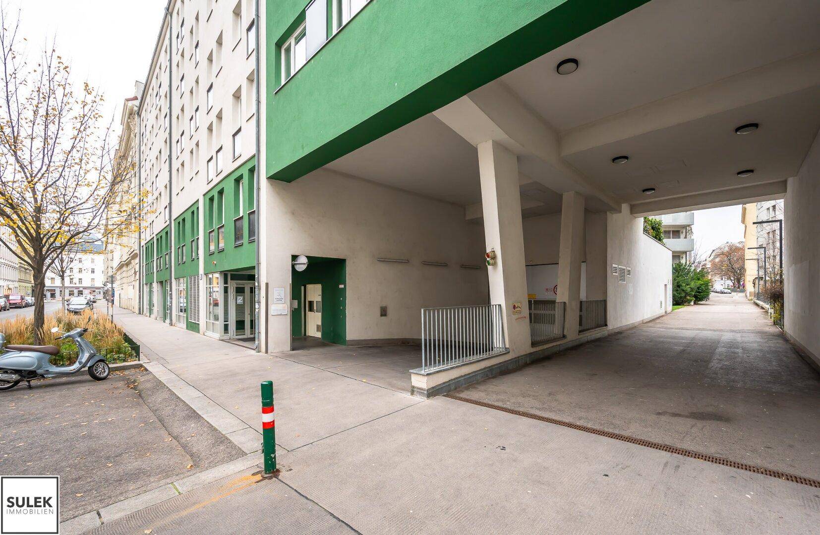 Überdachte Einfahrt zu einer Tiefgarage mit Säulen und Zugang zum Gebäude.