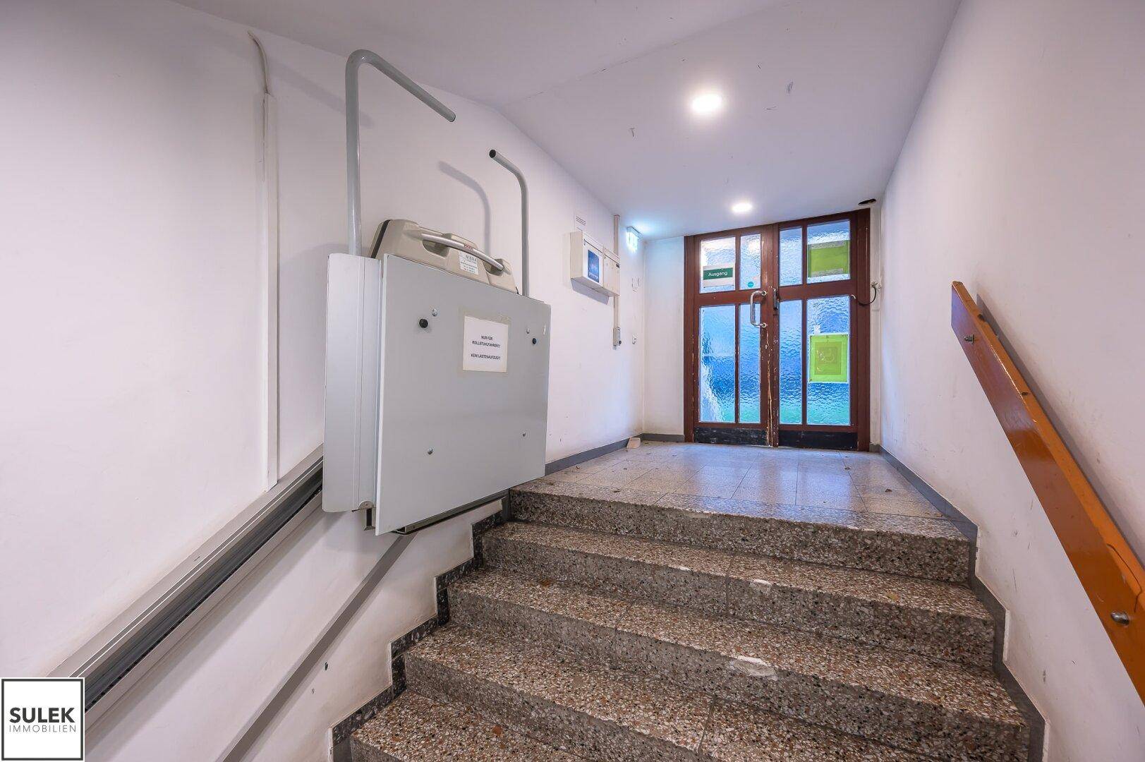 Treppenhaus mit Steinstufen und einem Treppenlift, der Barrierefreiheit für Rollstuhlfahrer bietet.