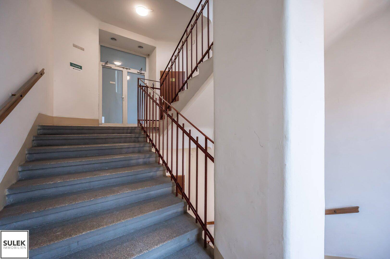 Geräumiges Treppenhaus mit Steinstufen und Metallgeländer, das zu den oberen Etagen führt.