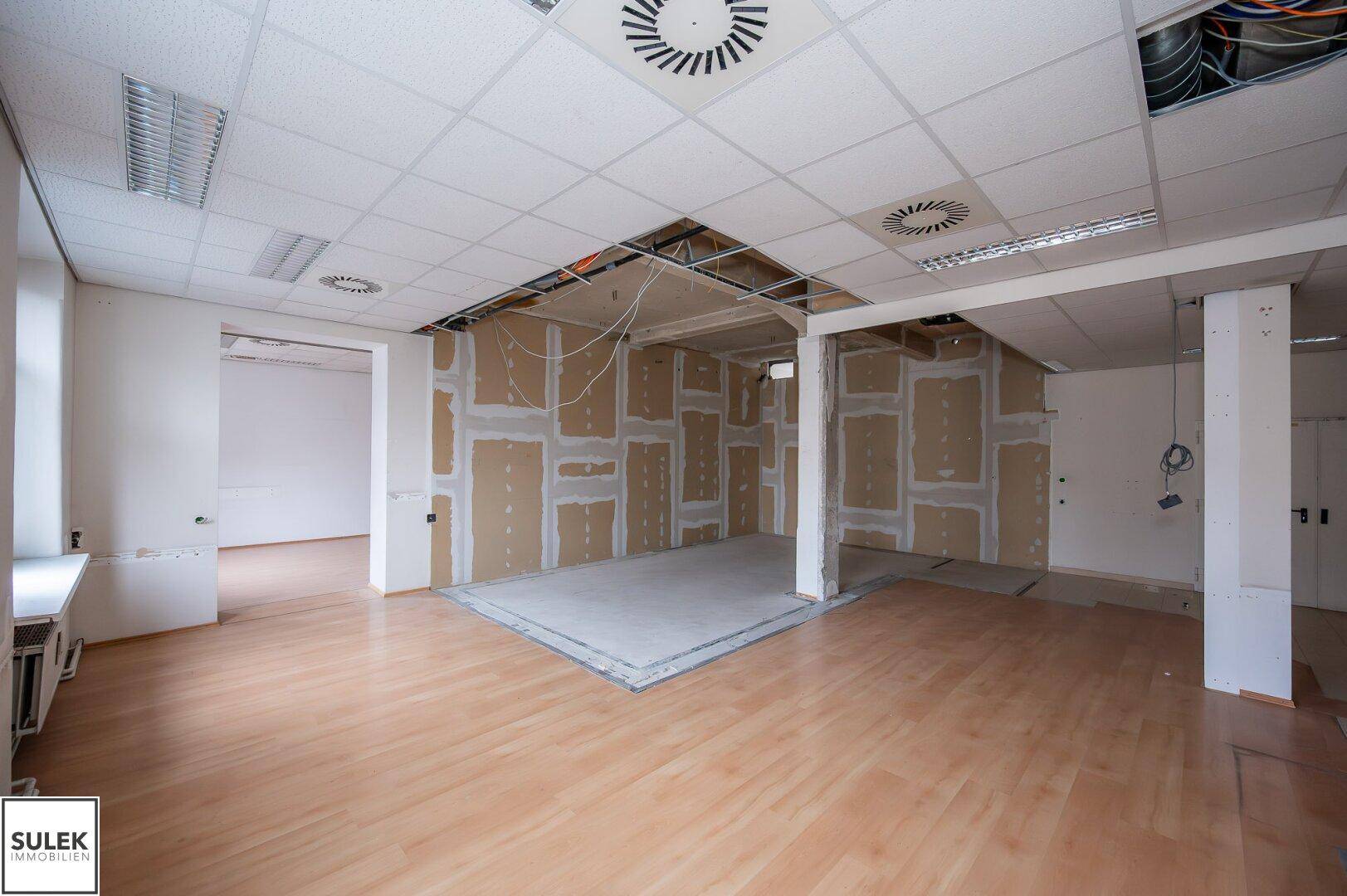 Büroraum mit freigelegter Decke und Trockenbauwänden, der sich in einem Zustand der Sanierung befindet.