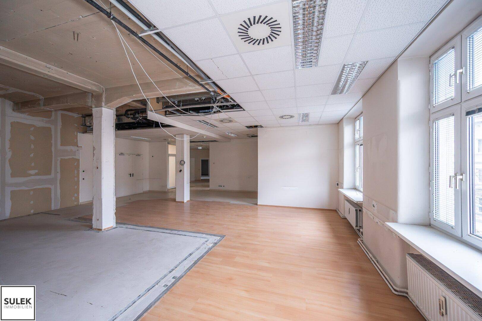 Großzügiger Bürobereich mit teilweise freigelegter Decke und unterschiedlichen Bodenbelägen, der renoviert wird.