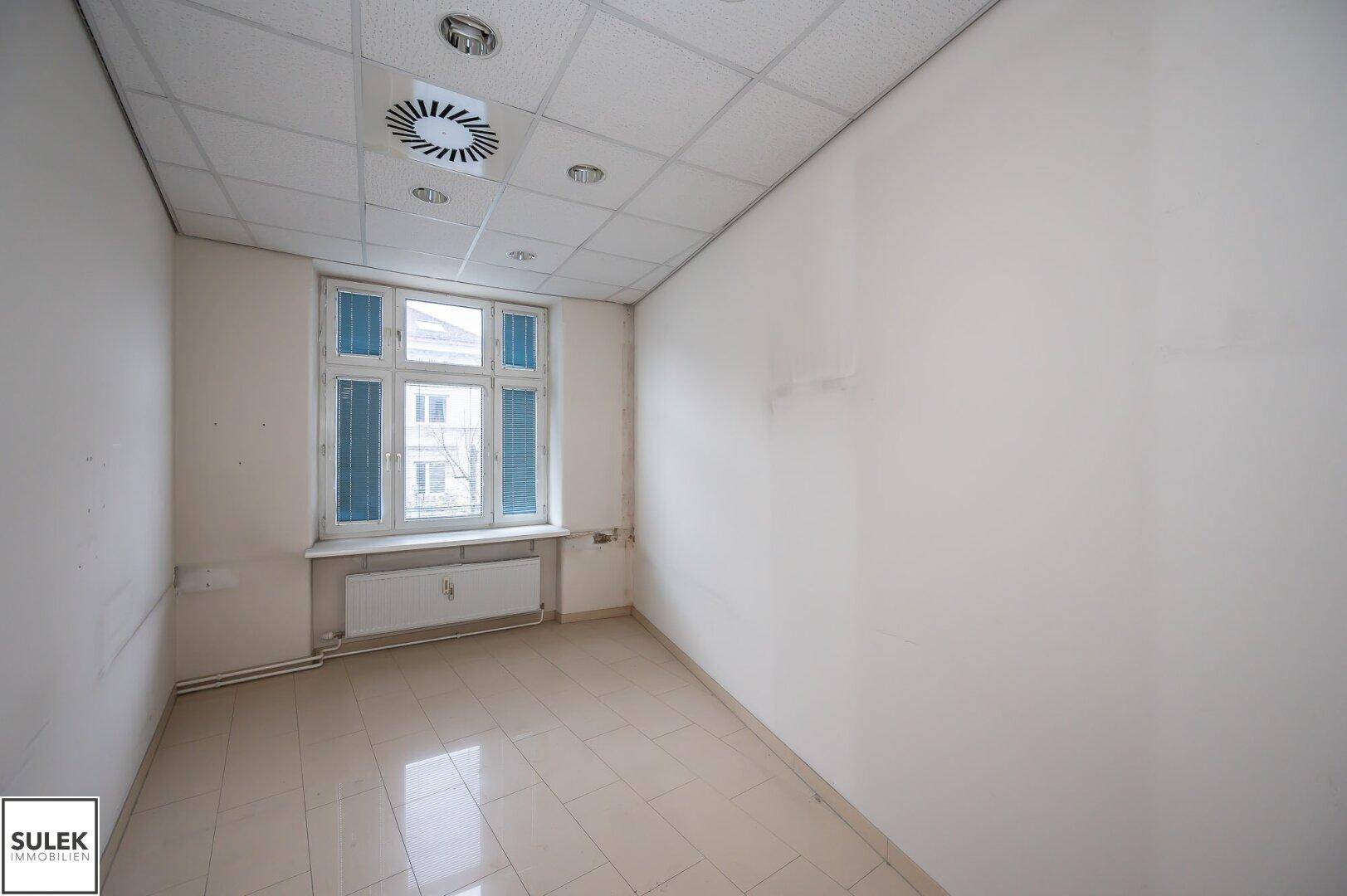 Kleiner Büroraum mit Fliesenboden, einem Fenster und abgehängter Decke, bereit zur Neugestaltung.