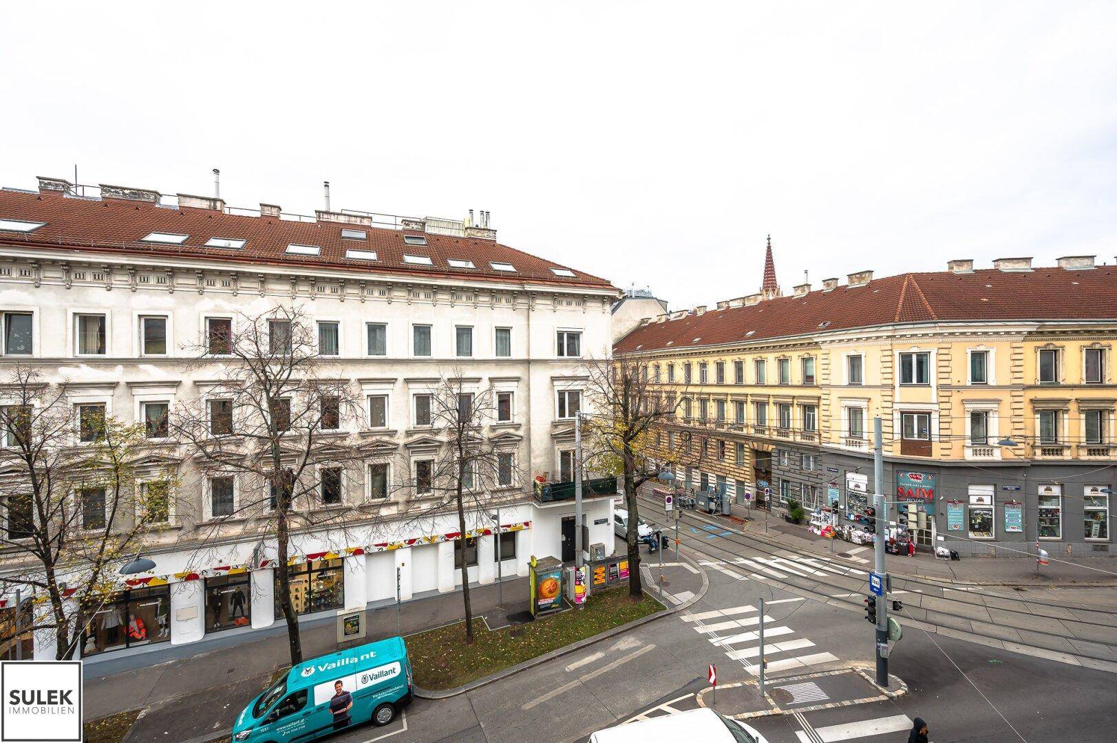 Panoramablick auf eine belebte Stadtstraße mit historischen Gebäuden und parkenden Fahrzeugen.