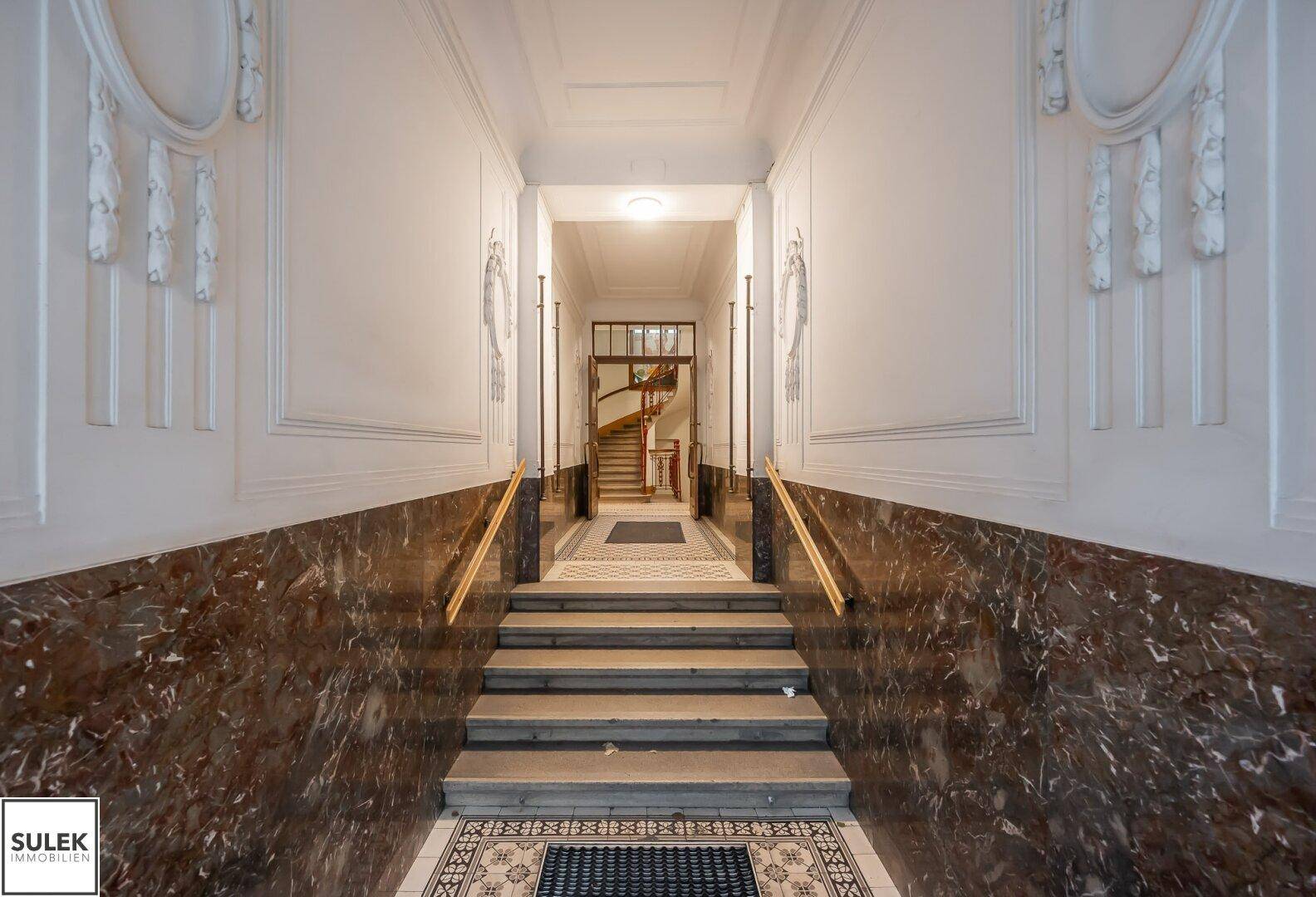 Elegante Eingangshalle mit Marmorverkleidung, hohen Decken und Blick auf das historische Treppenhaus.