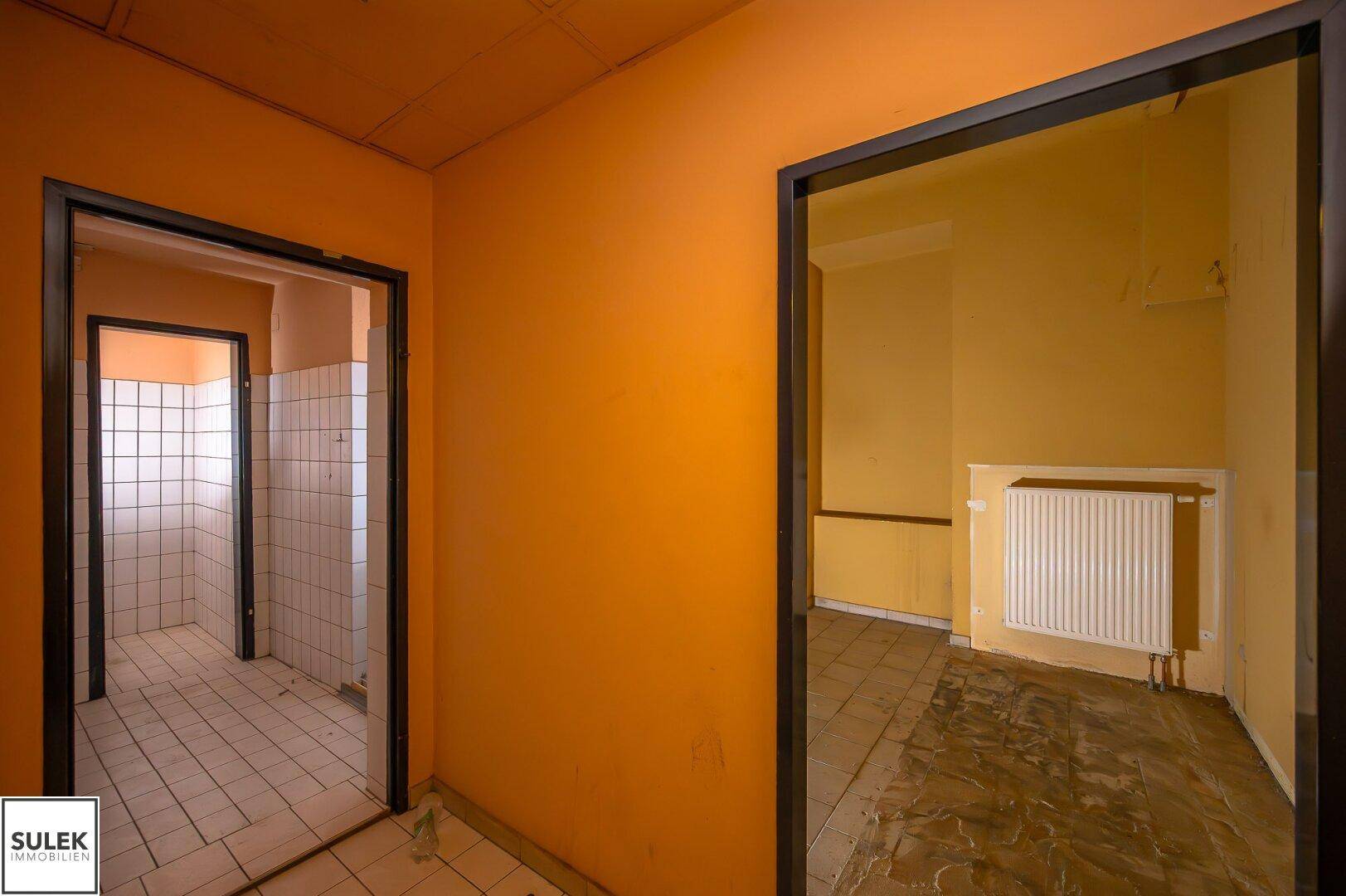 Flur in Renovierungszustand mit orangefarbenen Wänden und Blick auf einen gefliesten Sanitärbereich.