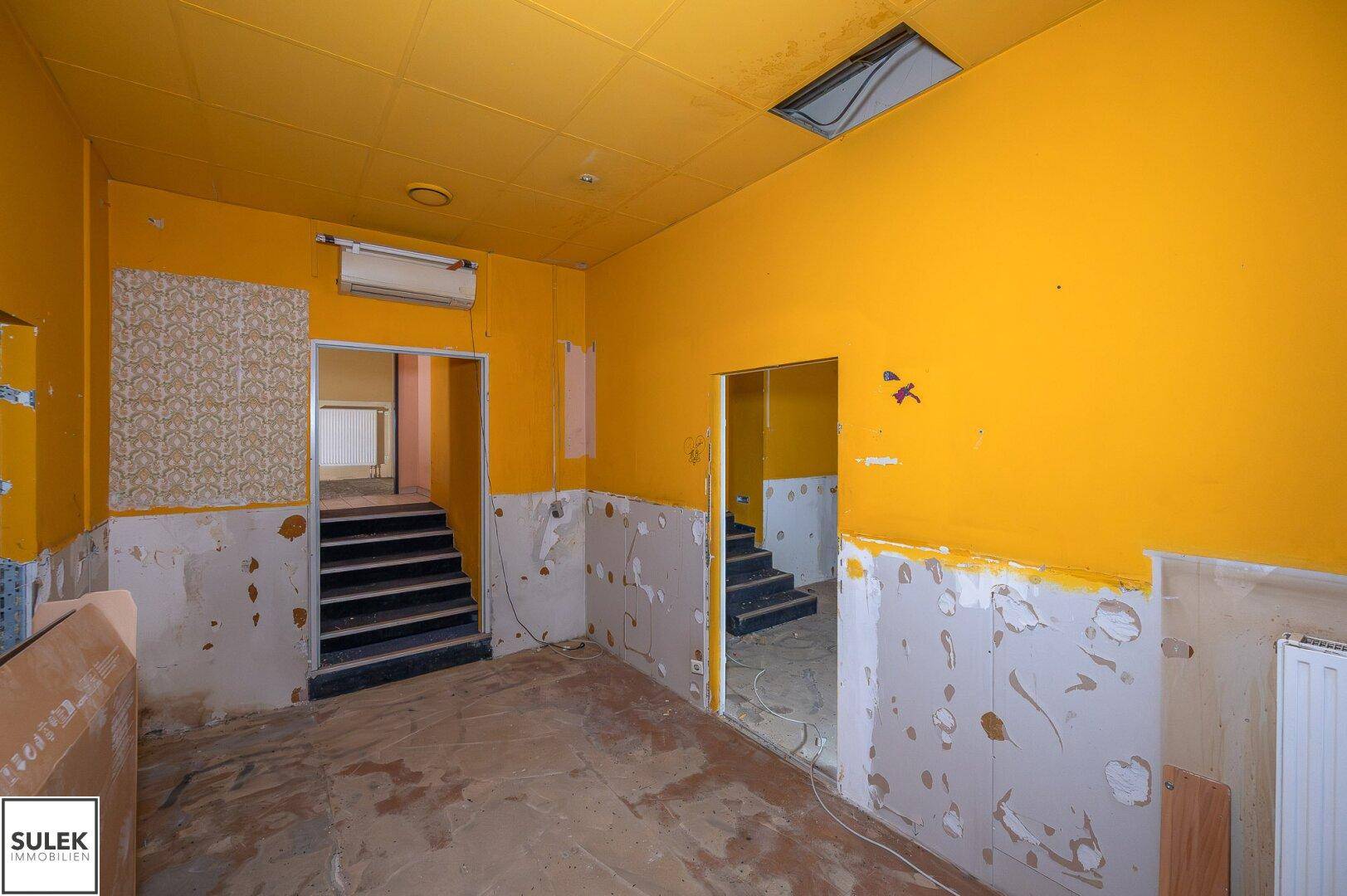 Renovierungsbedürftiger Raum mit gelben Wänden, freigelegten Wänden und Heizkörpern.