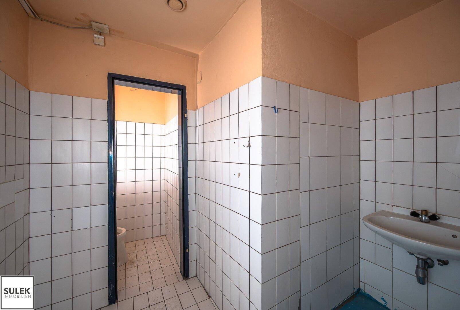Einfacher Toilettenraum in Renovierungszustand mit weißen Fliesenwänden und Waschbecken.