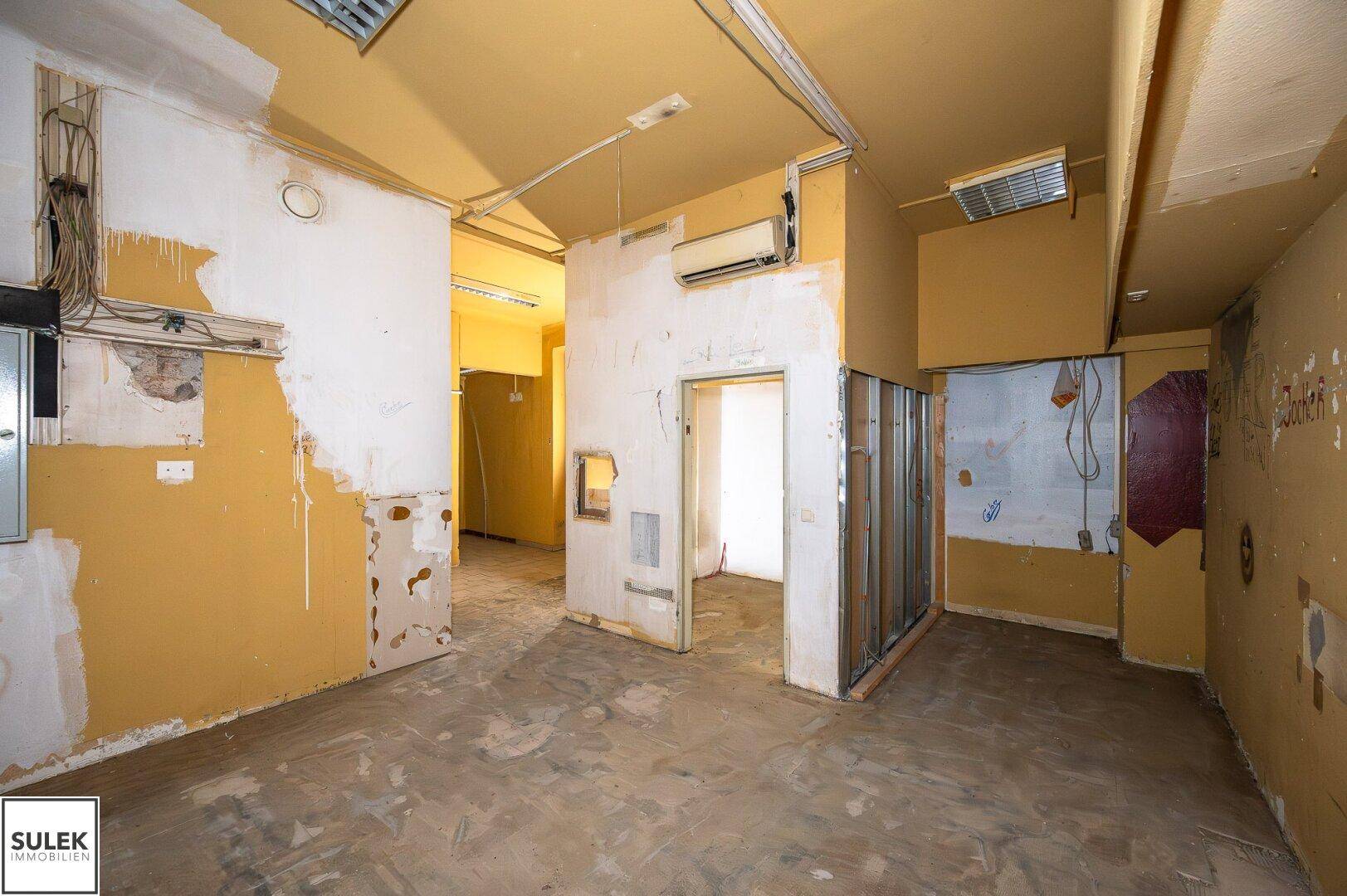 Großer Raum in Renovierungszustand mit teilweise freigelegten Wänden und sichtbaren Installationen.