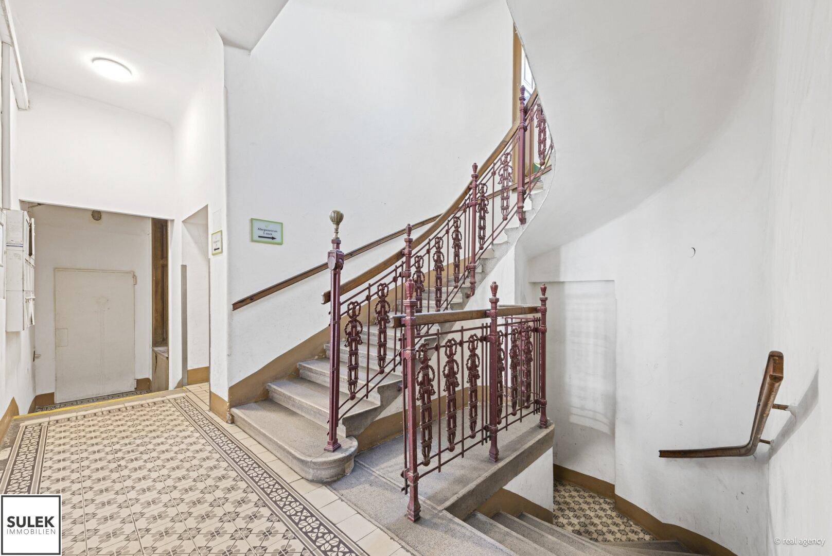 Historisches Treppenhaus mit kunstvollem Geländer und gemusterten Fliesenböden in einem Altbau.