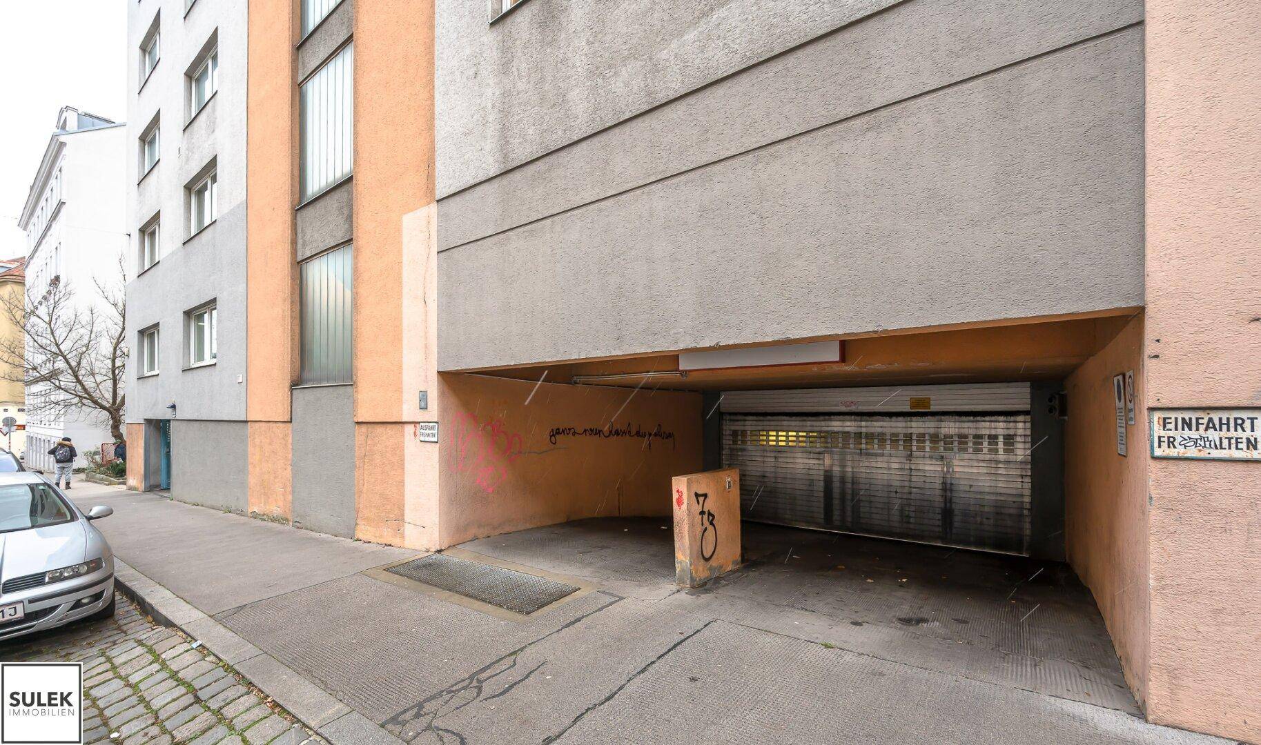 Gebäudeeingang mit Zufahrt zu einer Tiefgarage an einer städtischen Straße.