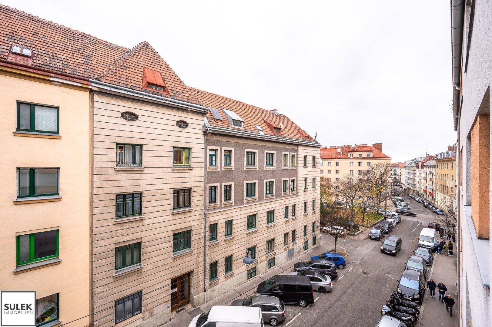 Städtische Straße mit parkenden Autos und historischen Gebäuden unter bewölktem Himmel.