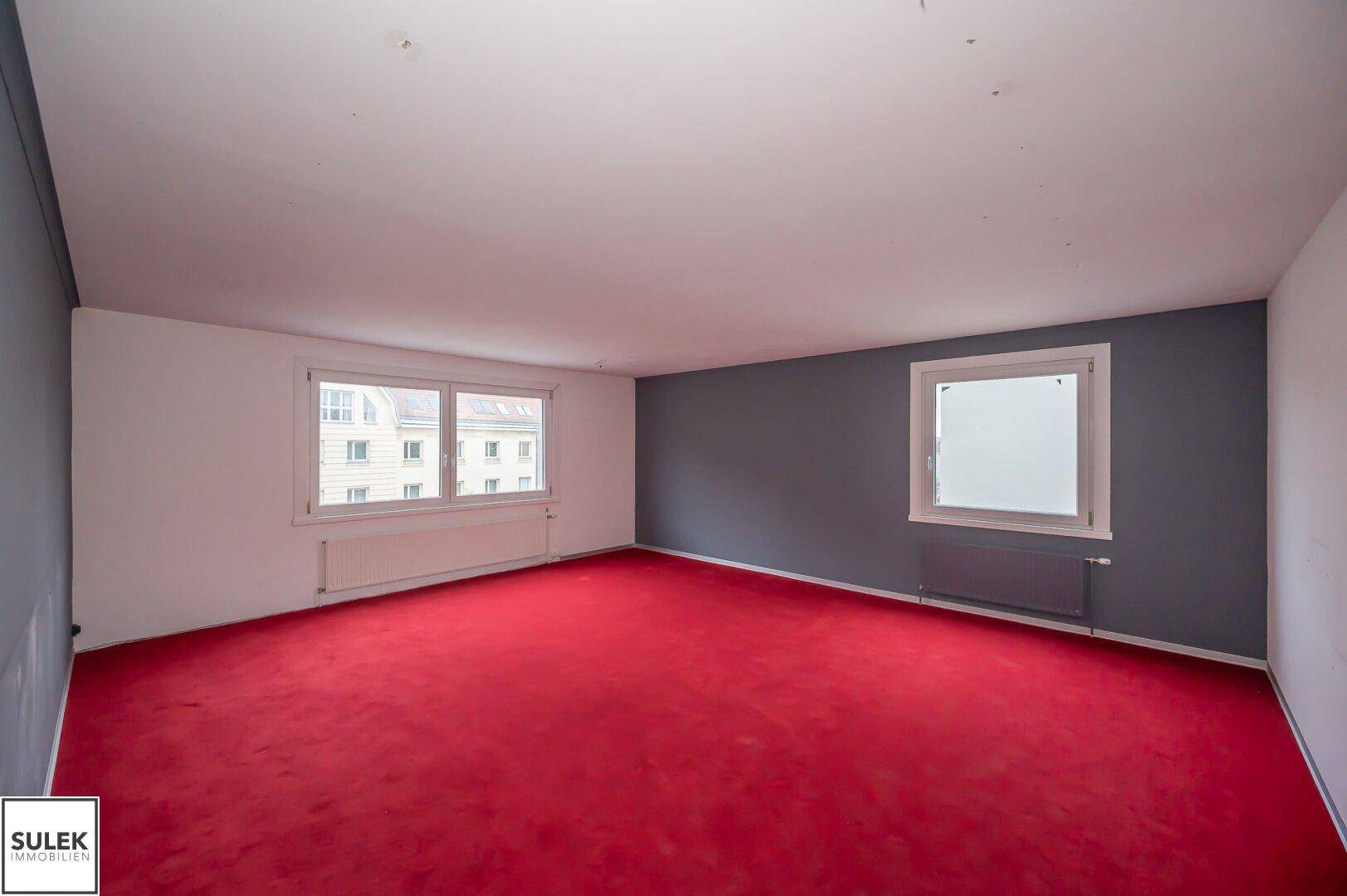 Geräumiger Raum mit leuchtend rotem Teppichboden und grauer Akzentwand, bereit zur Nutzung.