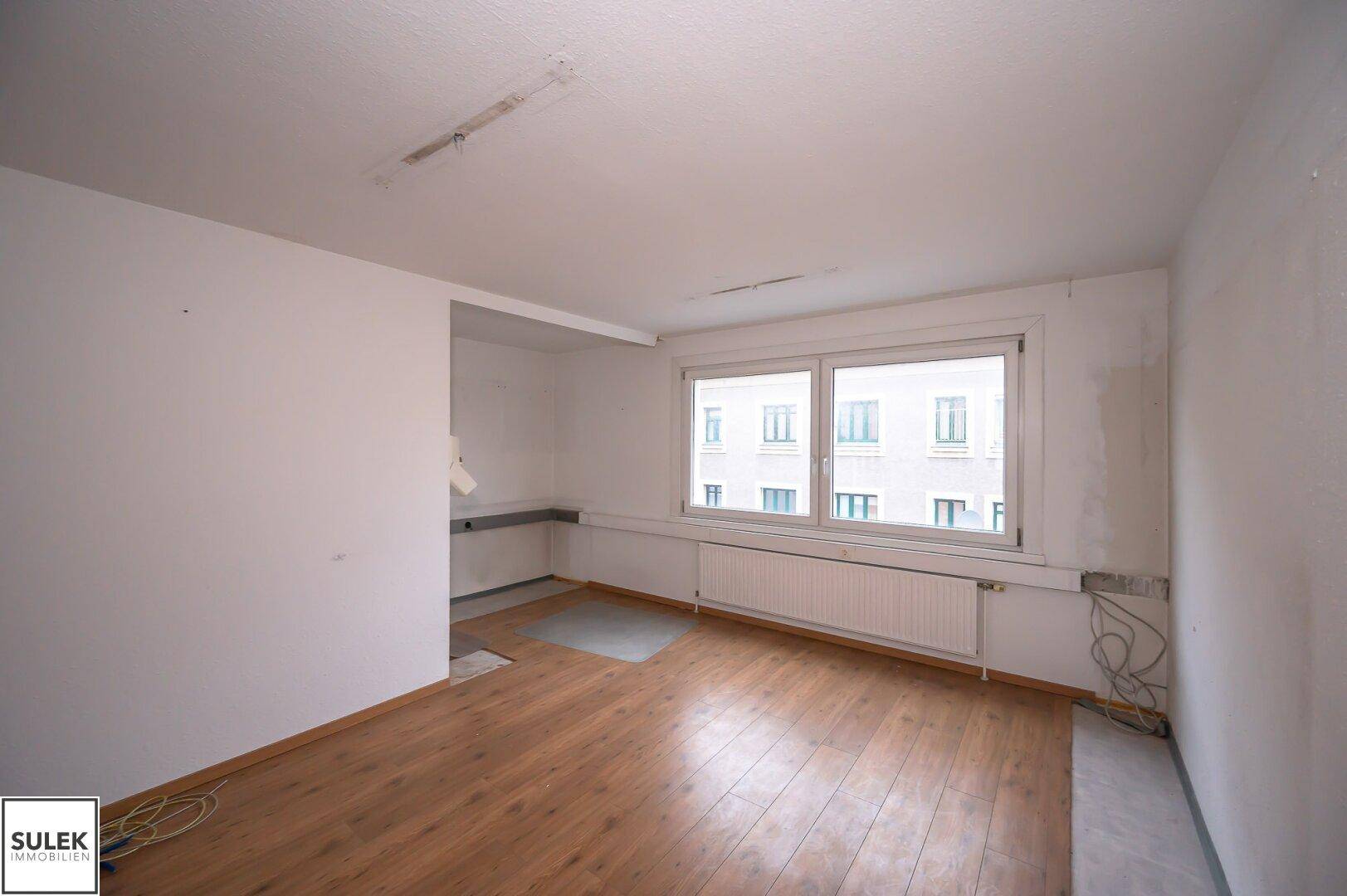 Raum mit gemischtem Bodenbelag und einem großen Fenster, das viel natürliches Licht hereinlässt.